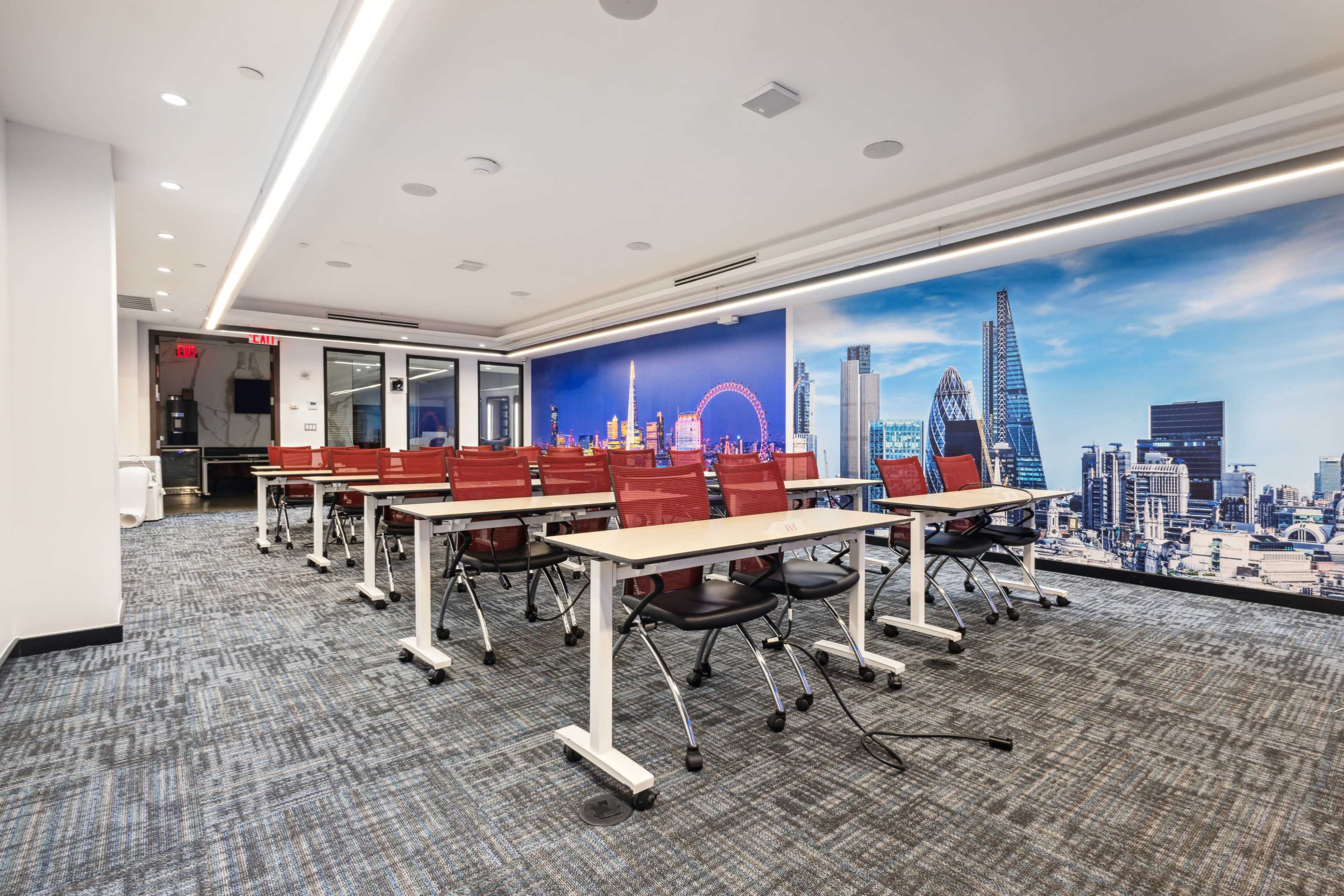 A modern conference room features rows of red and black chairs paired with white tables, set against a backdrop of a city skyline mural.
