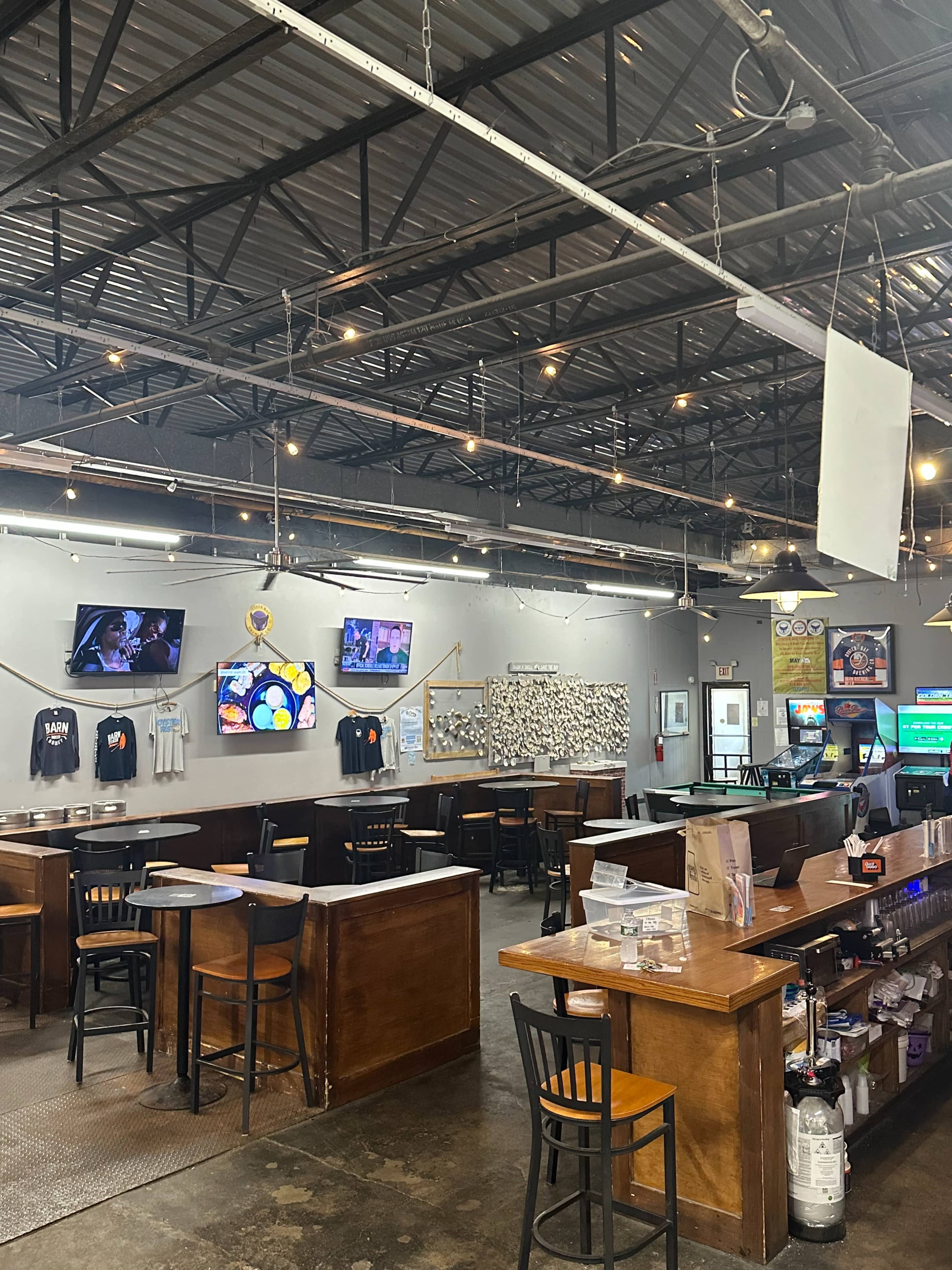The interior of a casual bar features wooden tables and chairs, multiple televisions mounted on the walls, and a bar with various items for service.