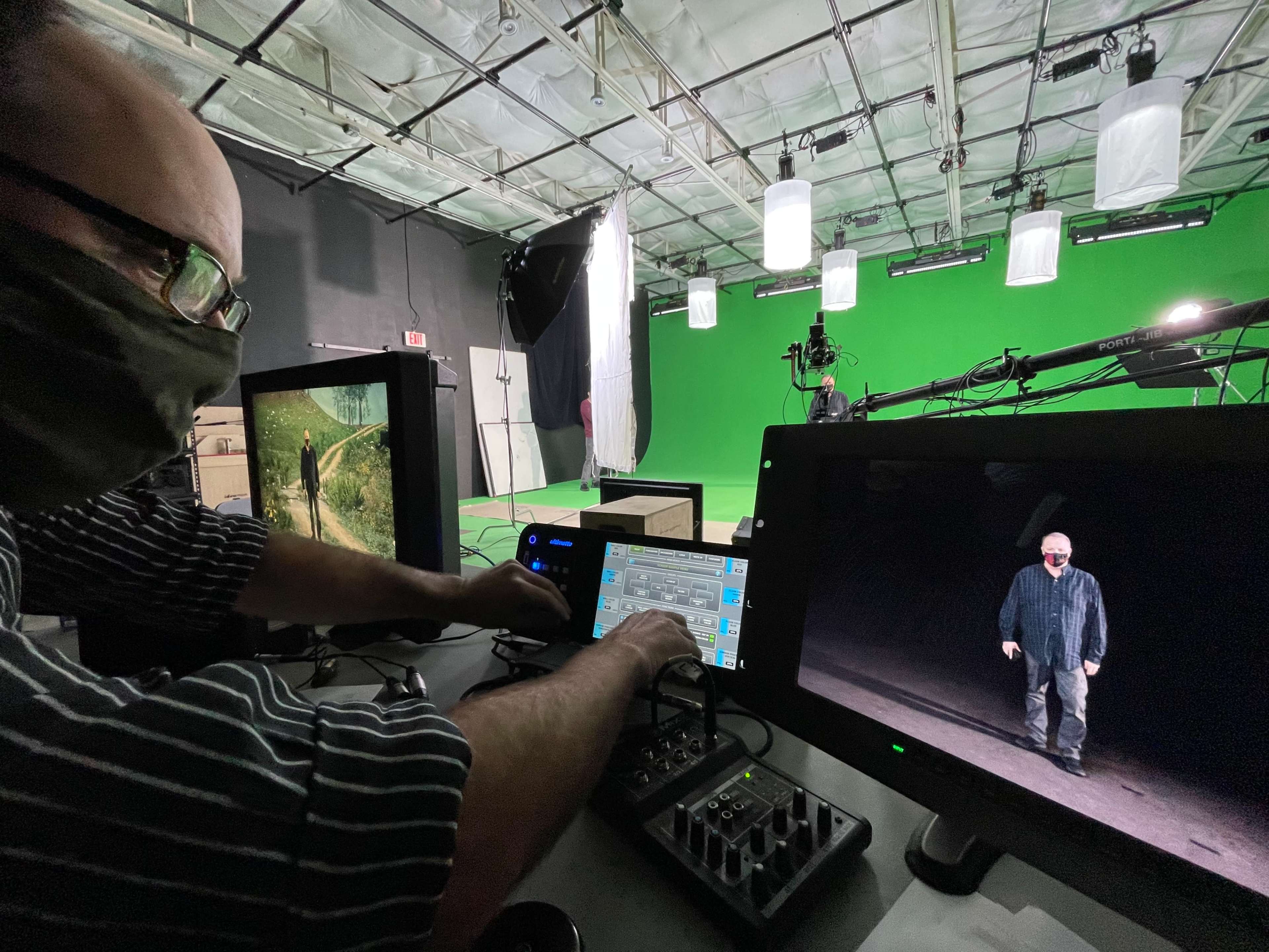 A person operates a control panel in a studio with green screens and lighting equipment.