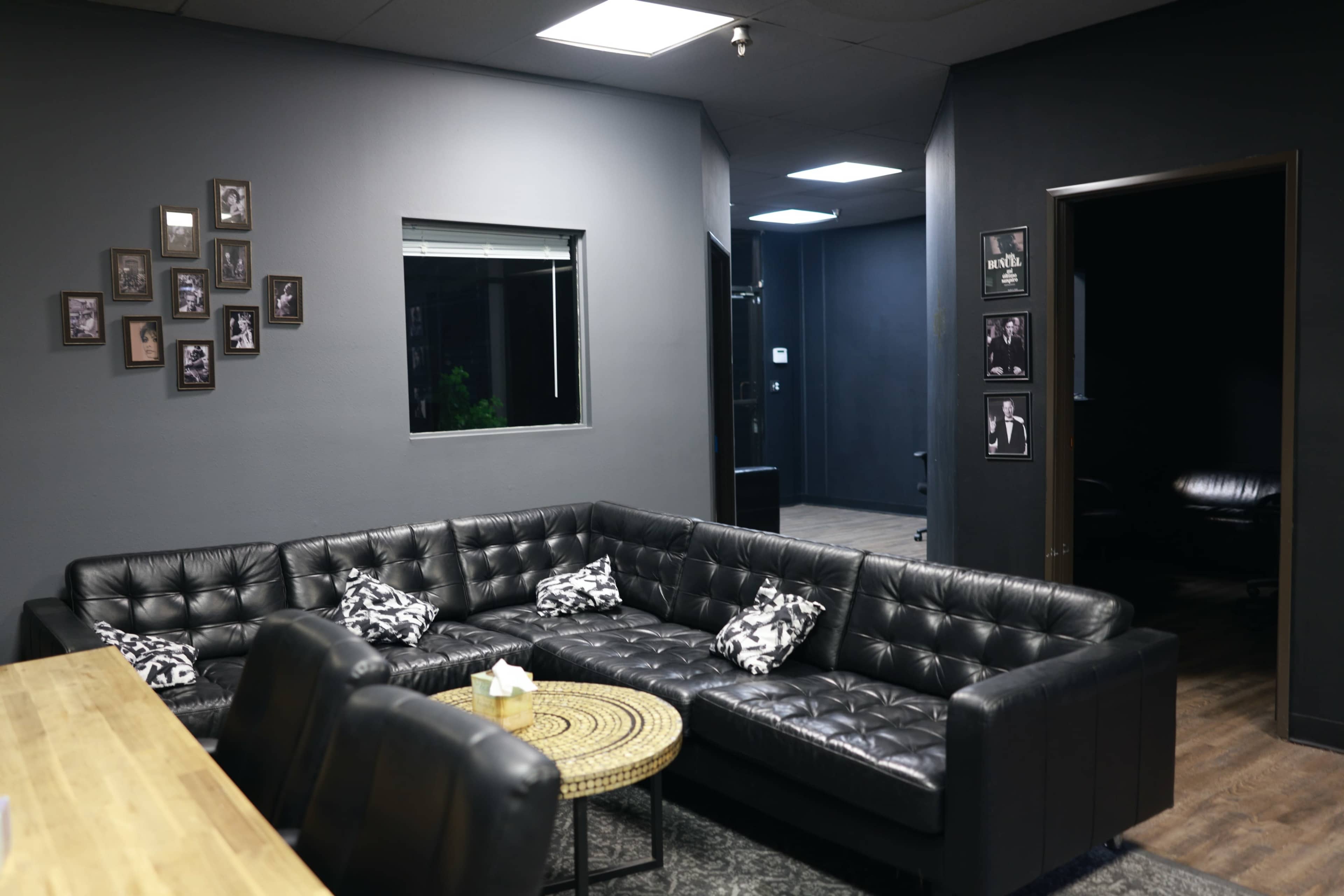 A modern lounge area with a black leather sectional sofa, a round coffee table, and framed photographs on the gray walls.