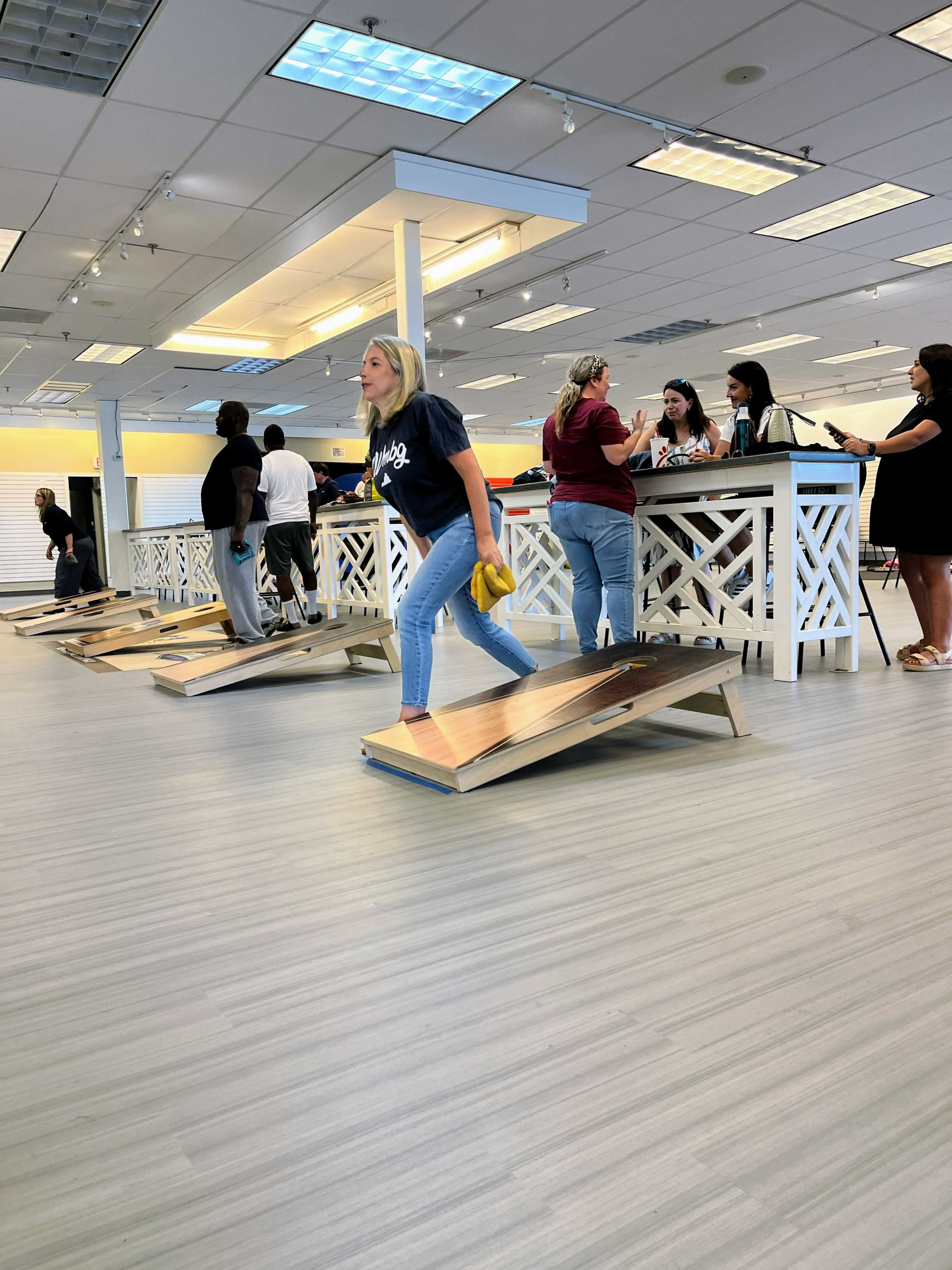 A woman in a navy shirt walks on a wooden ramp inside a brightly lit store where people are gathered at a counter.