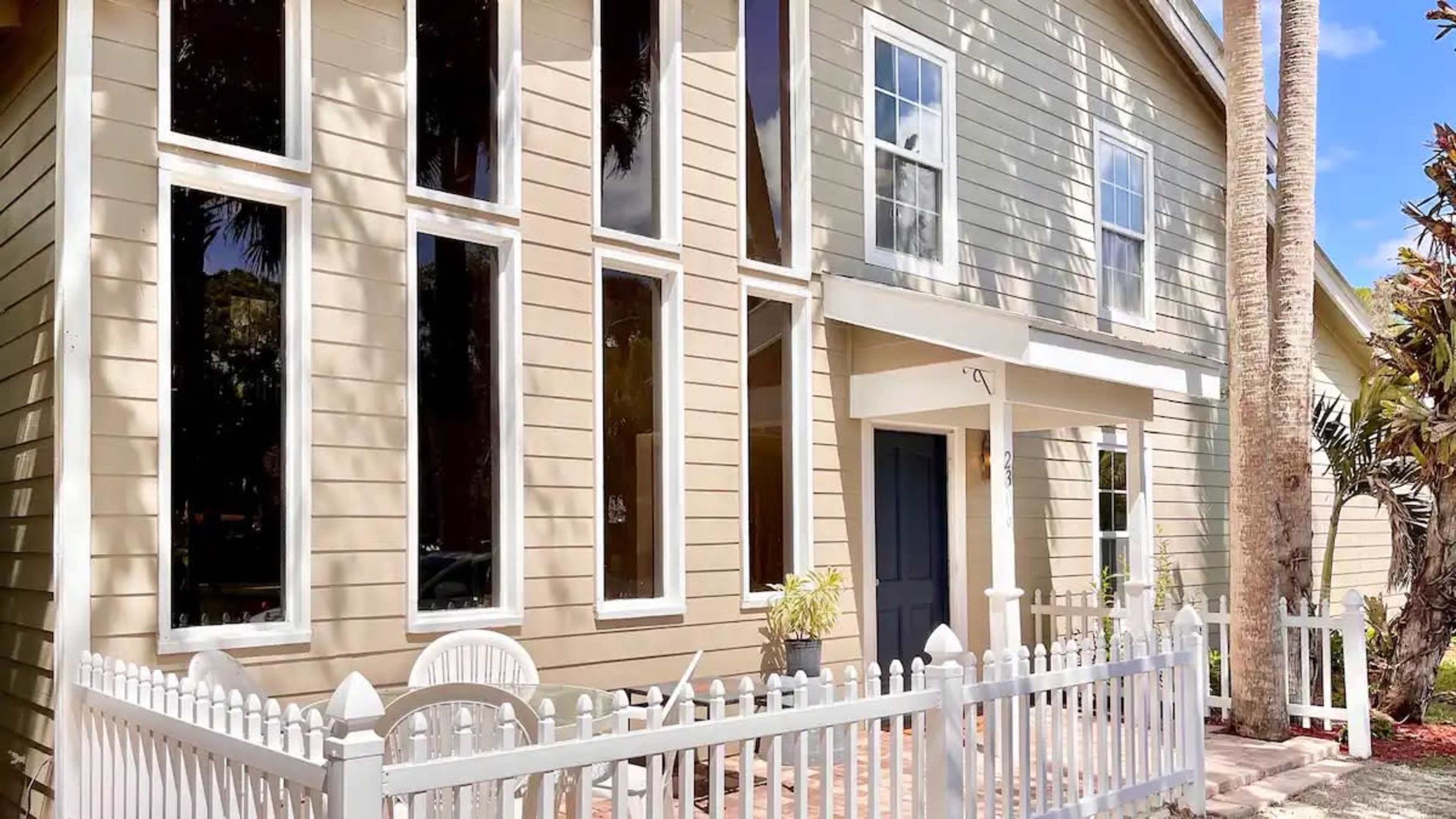 A two-story house with large windows and a white picket fence surrounding a front patio area.