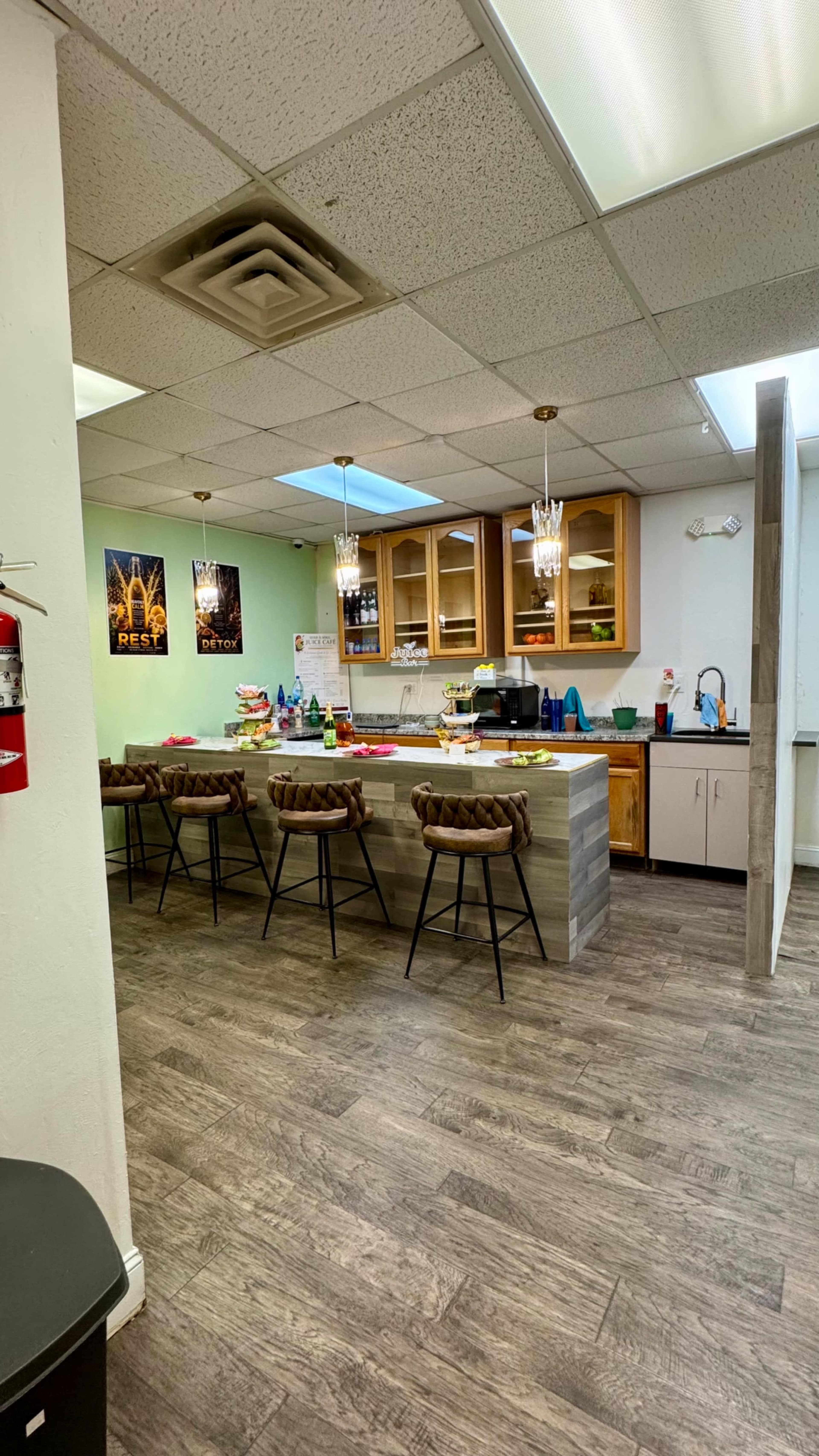 The image shows a modern kitchen area with wooden cabinets, a countertop with several bar stools, and various items scattered on the surface.
