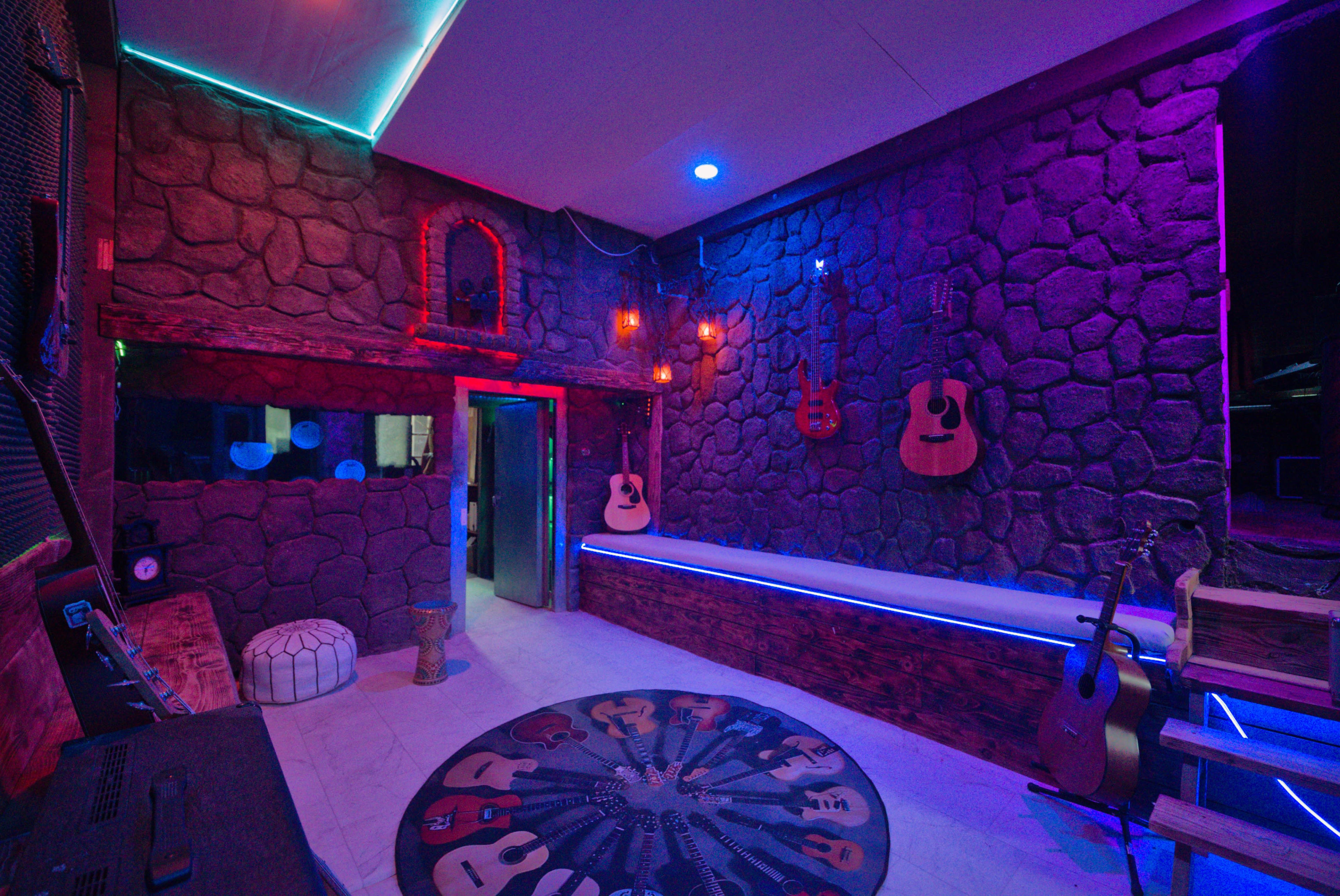 The image shows a vibrant music studio with stone walls, colorful lighting, and acoustic guitars hanging on the walls.