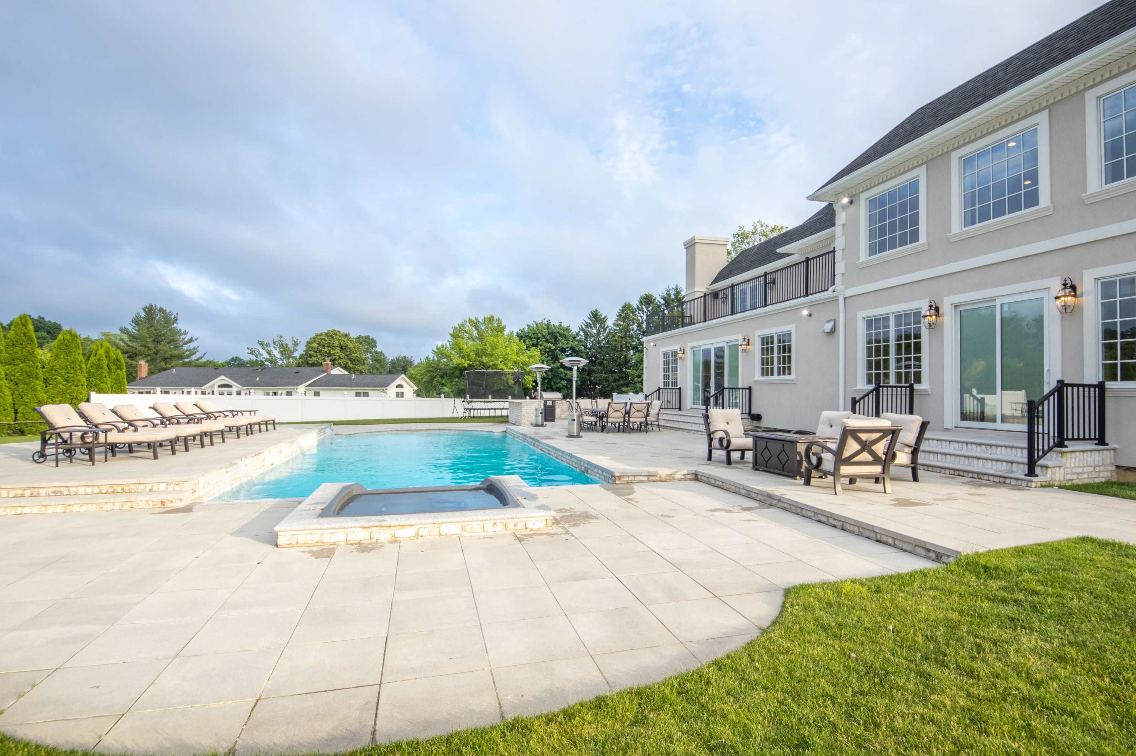 A spacious backyard features a swimming pool surrounded by lounge chairs and a patio area connected to a large house.
