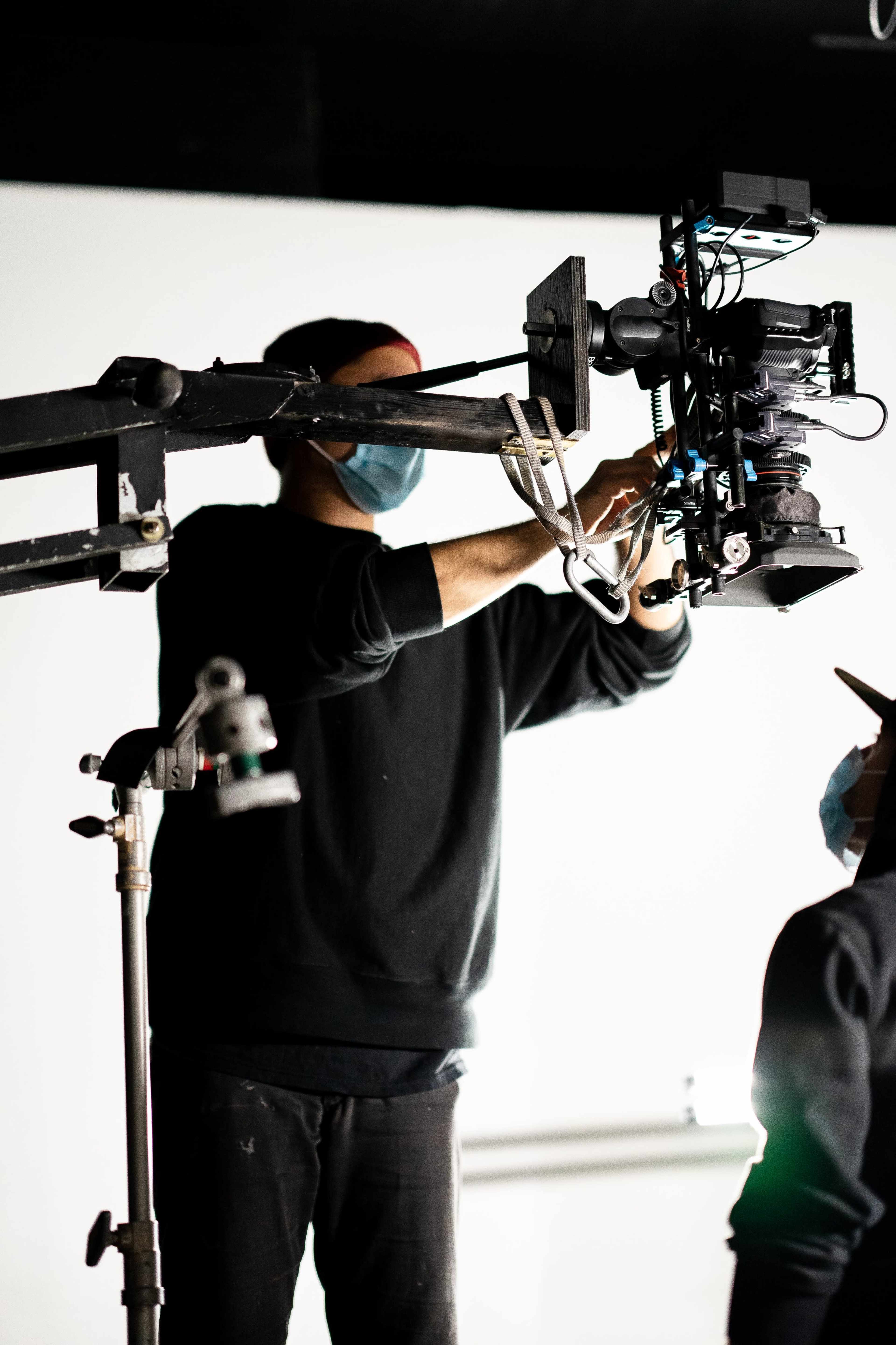 A person adjusts a camera mounted on a crane in a studio setting.