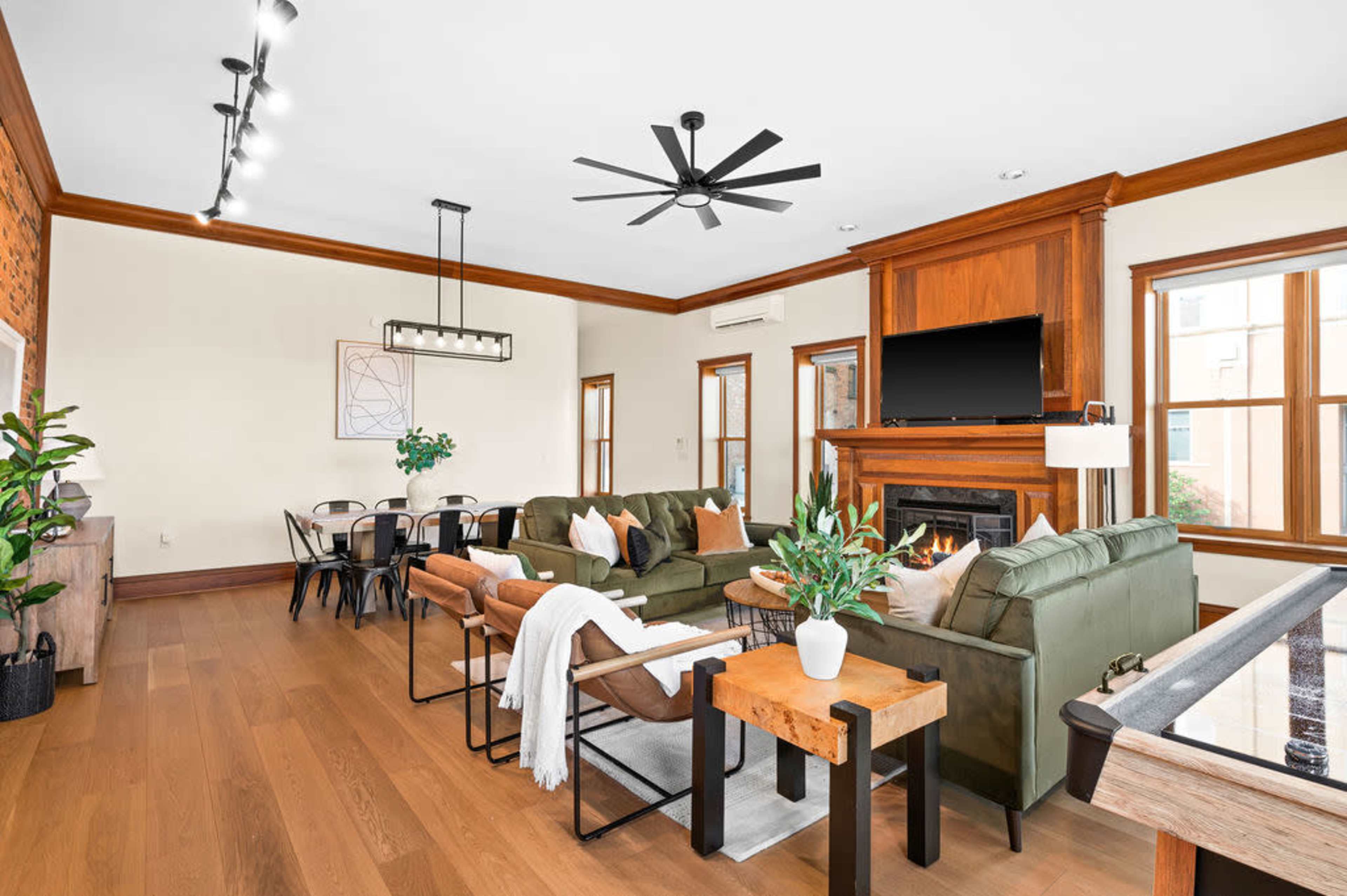 A spacious living room features a fireplace, dark wood accents, comfortable seating, and a dining area with a large table.
