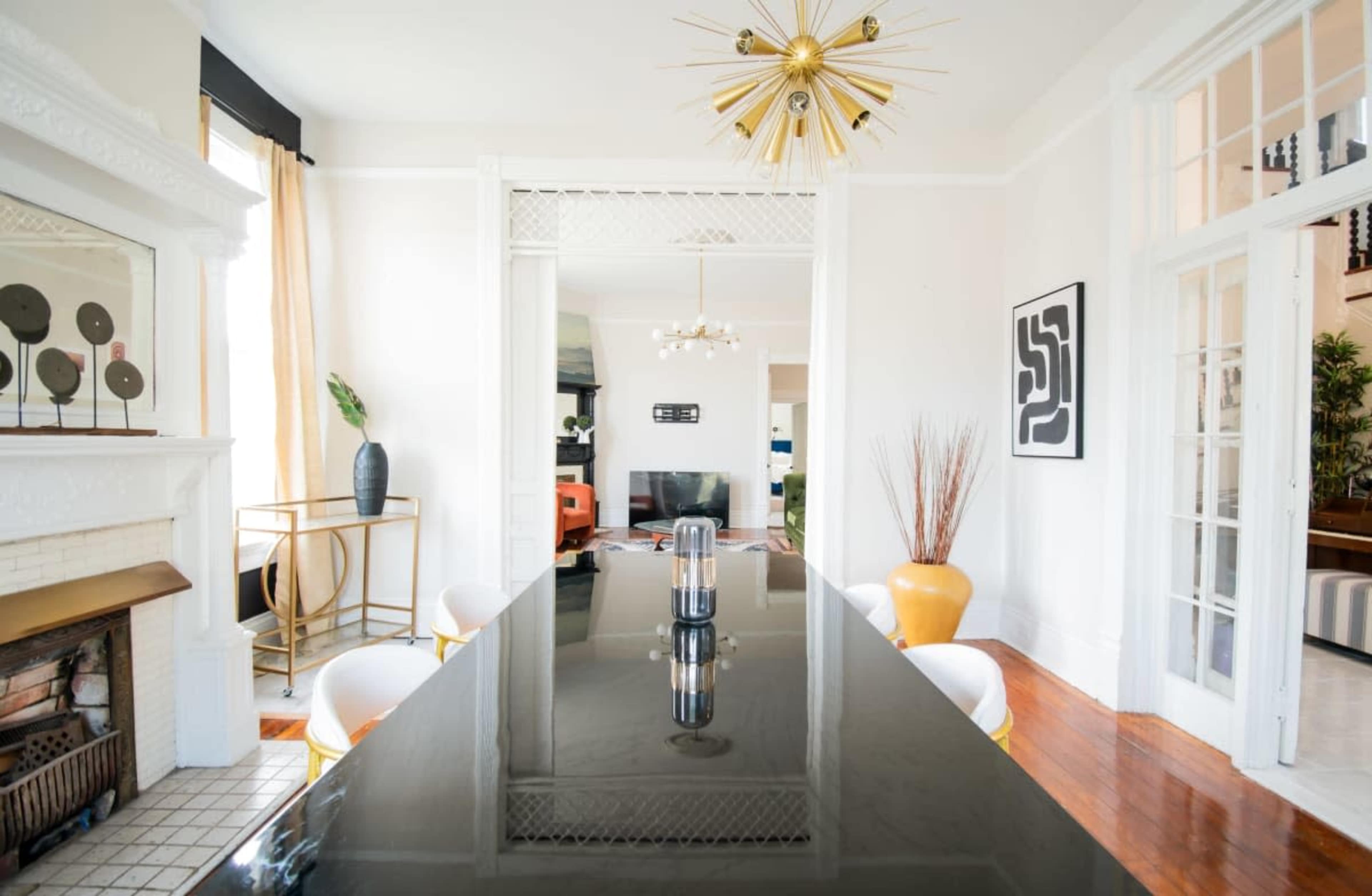 A long black dining table is positioned in a bright room featuring a decorative fireplace and modern furniture.