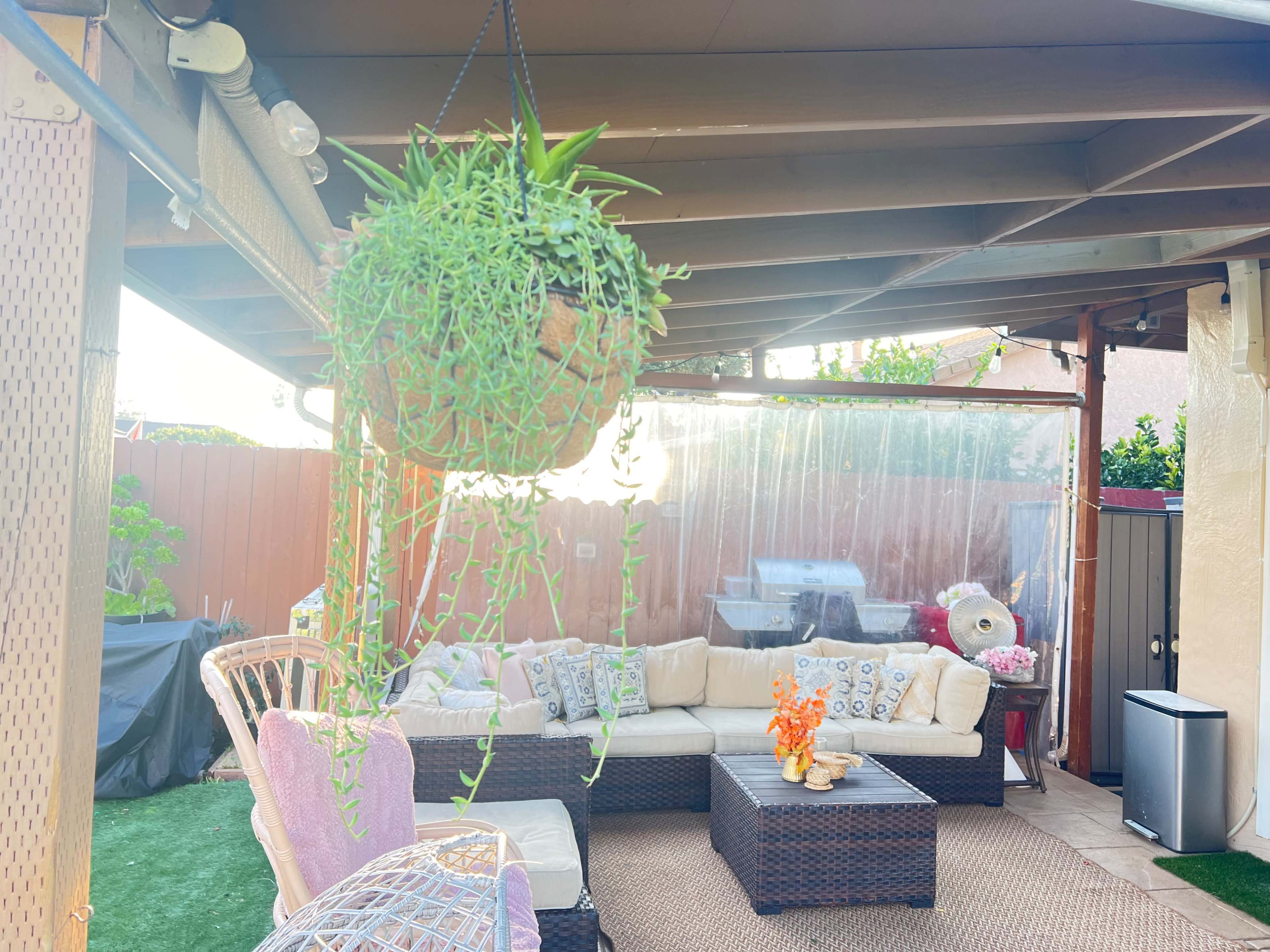 A backyard patio area with a hanging plant, outdoor seating, and a table adorned with decorative items.