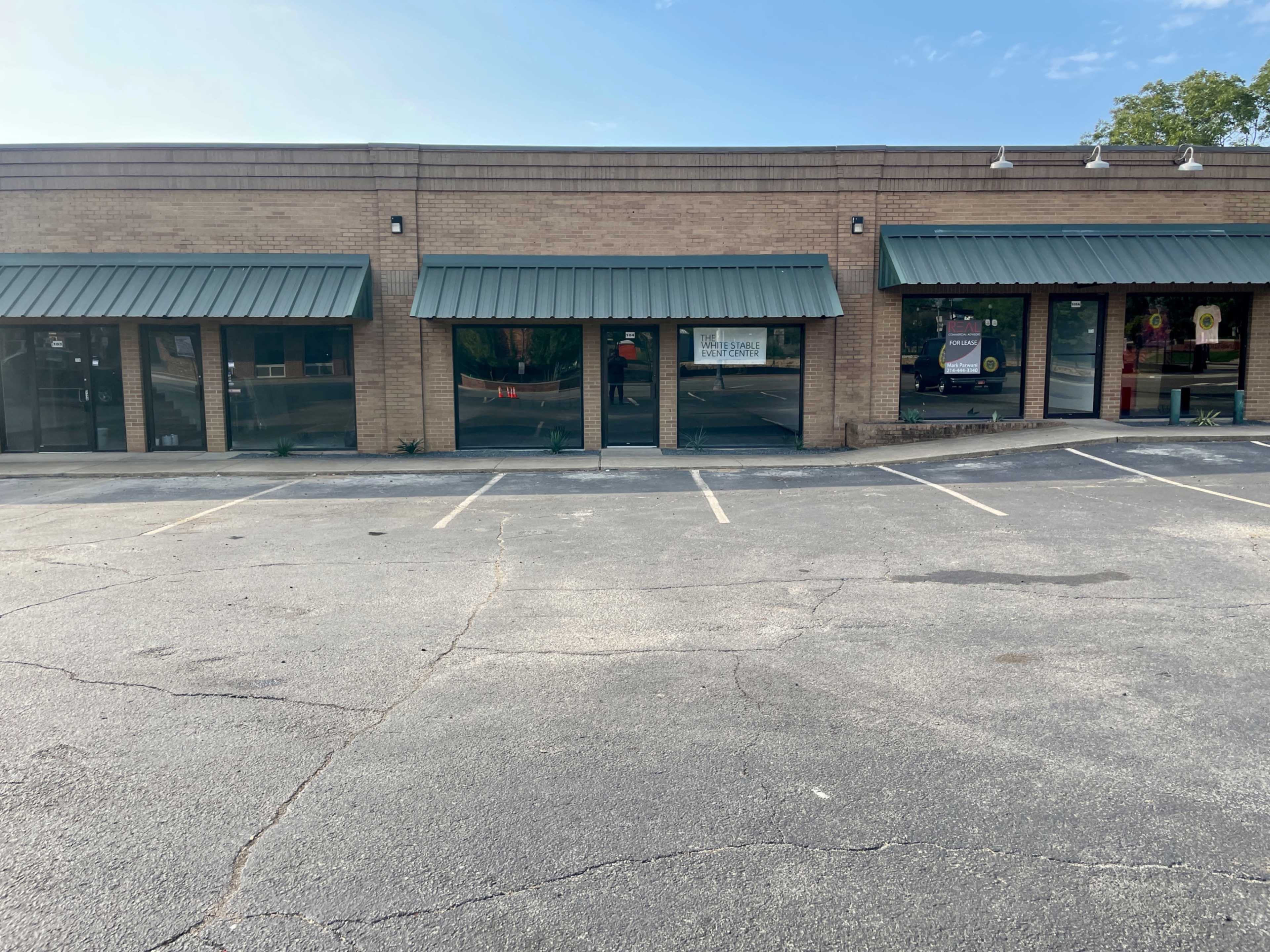 A commercial building with several storefronts featuring green awnings and empty parking spaces in front.