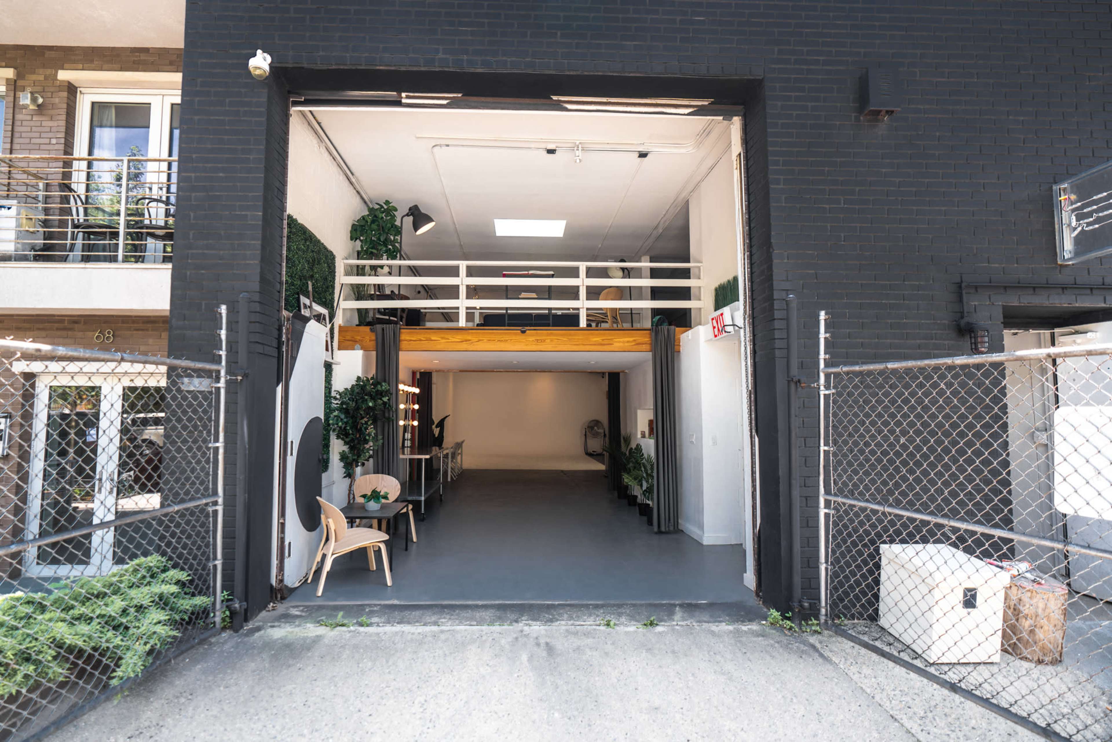 The open entrance of a modern industrial space with a minimalist interior, framed by a black exterior wall and a chain-link fence.