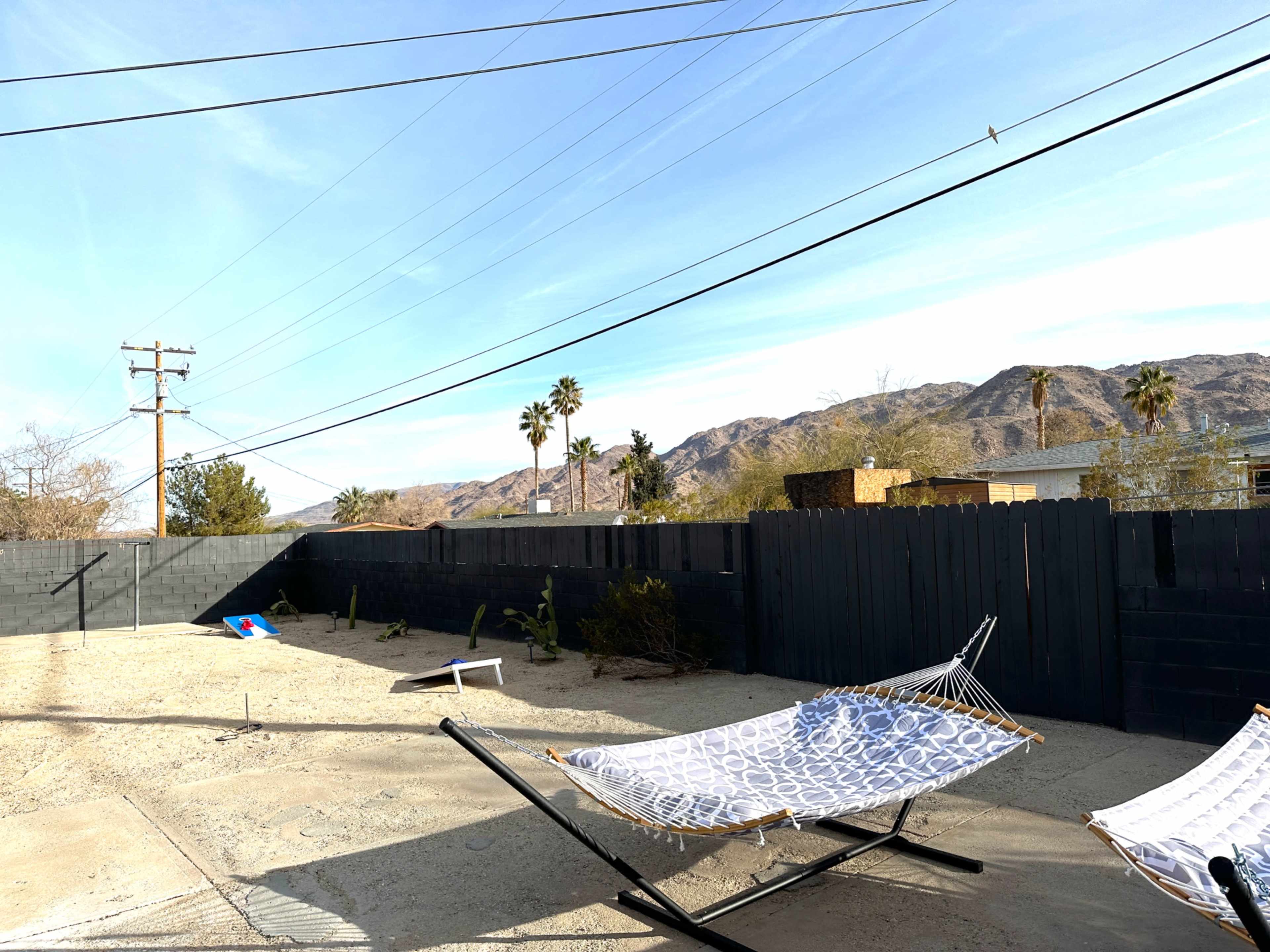 A vacant backyard features two hammocks, desert vegetation, and mountains in the background under a clear sky.