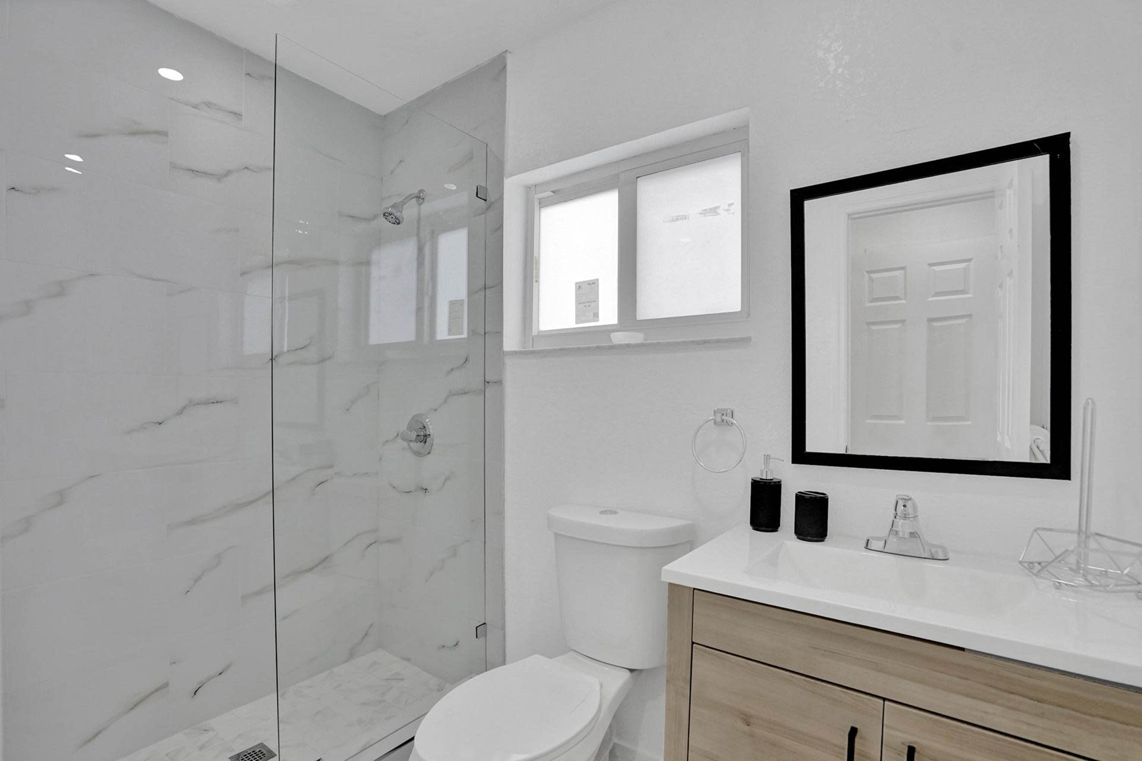 A modern bathroom with a glass shower, a toilet, a sink with a cabinet, and a large mirror.