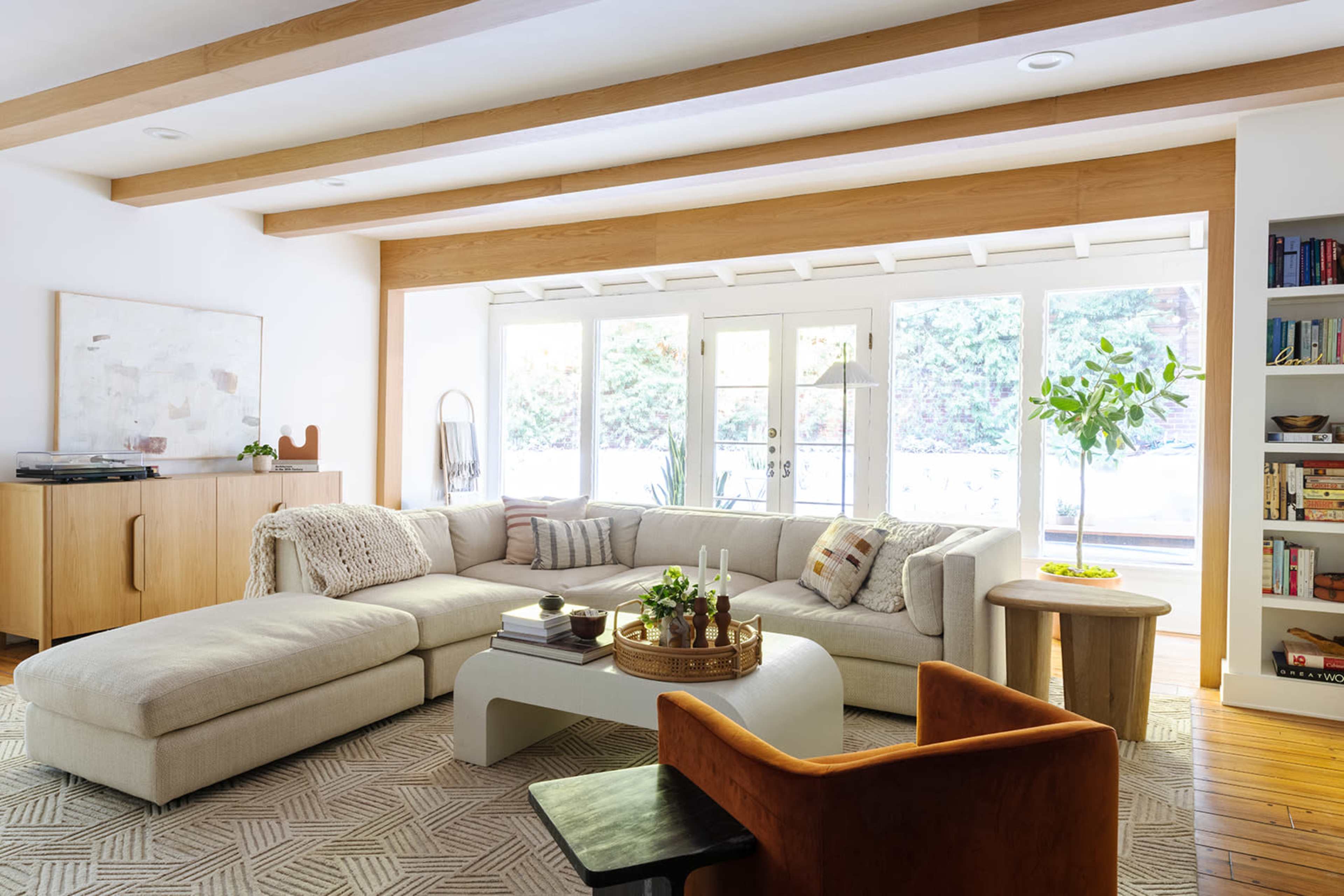 A spacious living room features a large sectional sofa, a round coffee table with plants, and a wall of windows that offers natural light.
