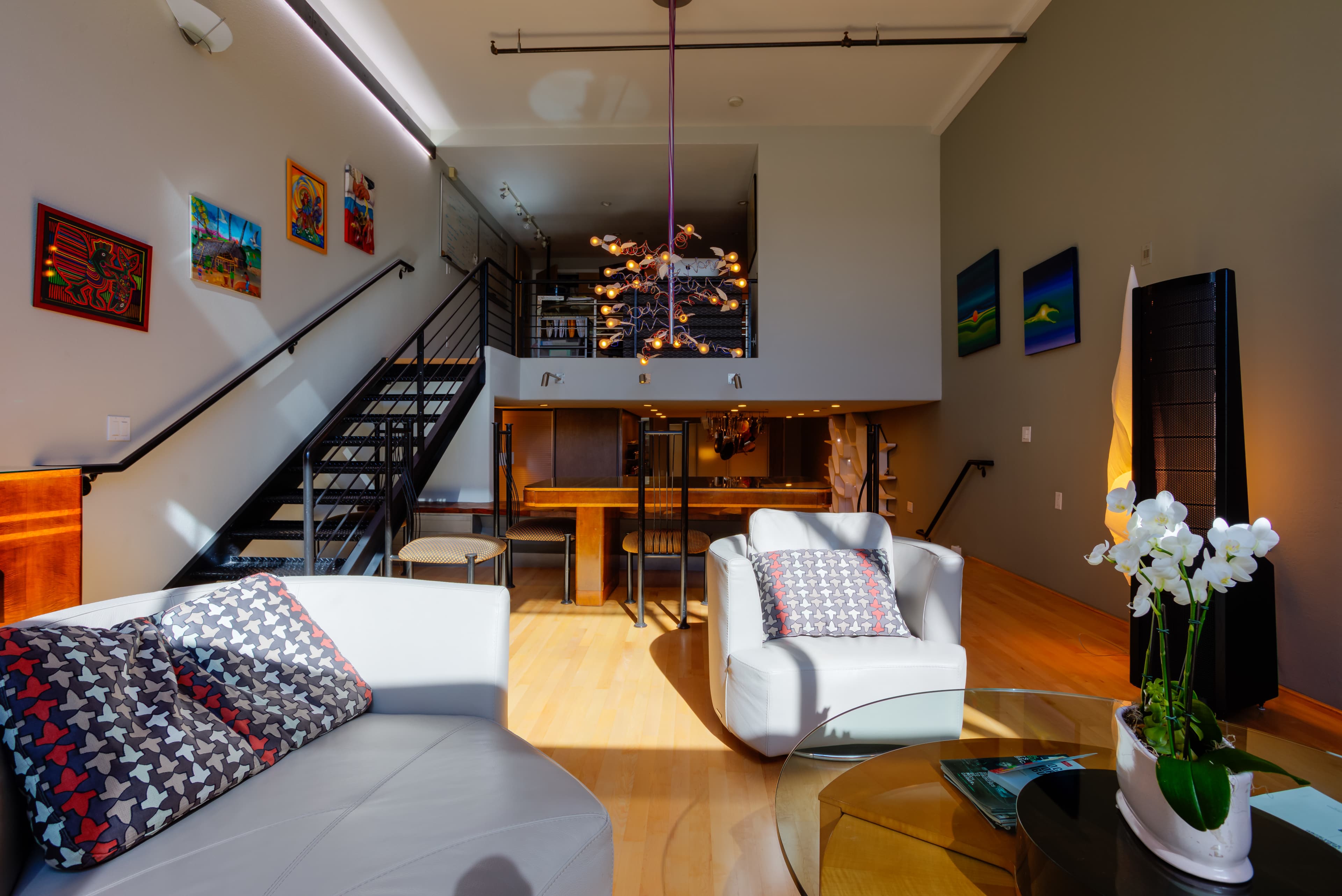 A modern living space with a staircase, large windows, a dining area, and contemporary furniture.