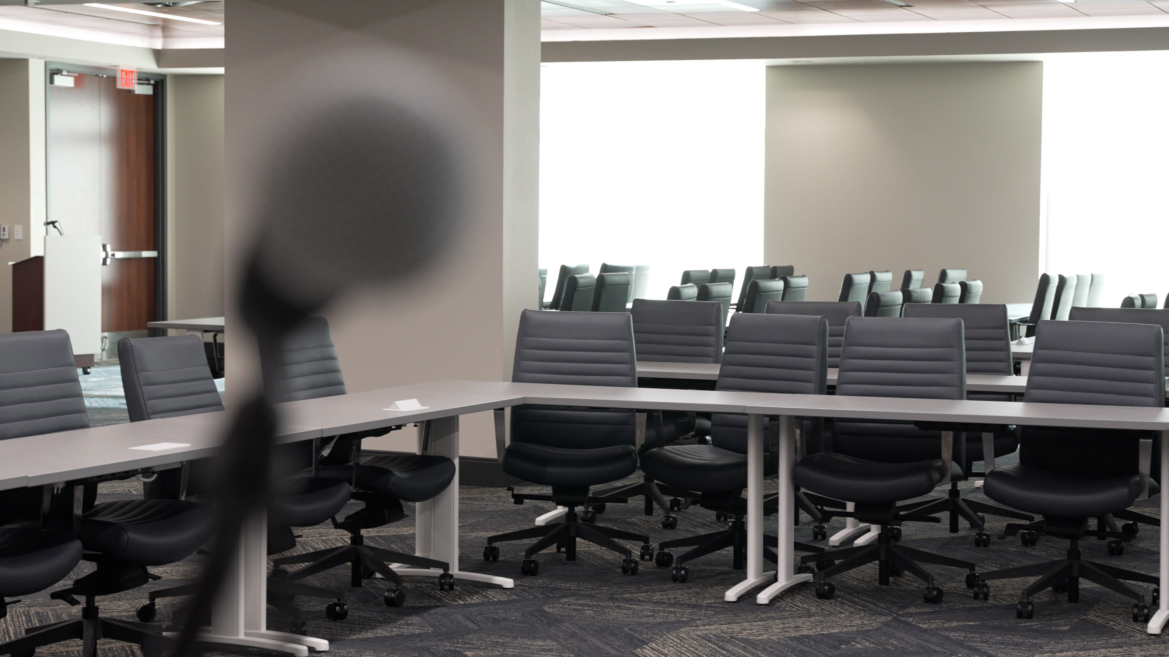 A conference room with a large table and multiple gray office chairs is set up for a meeting.