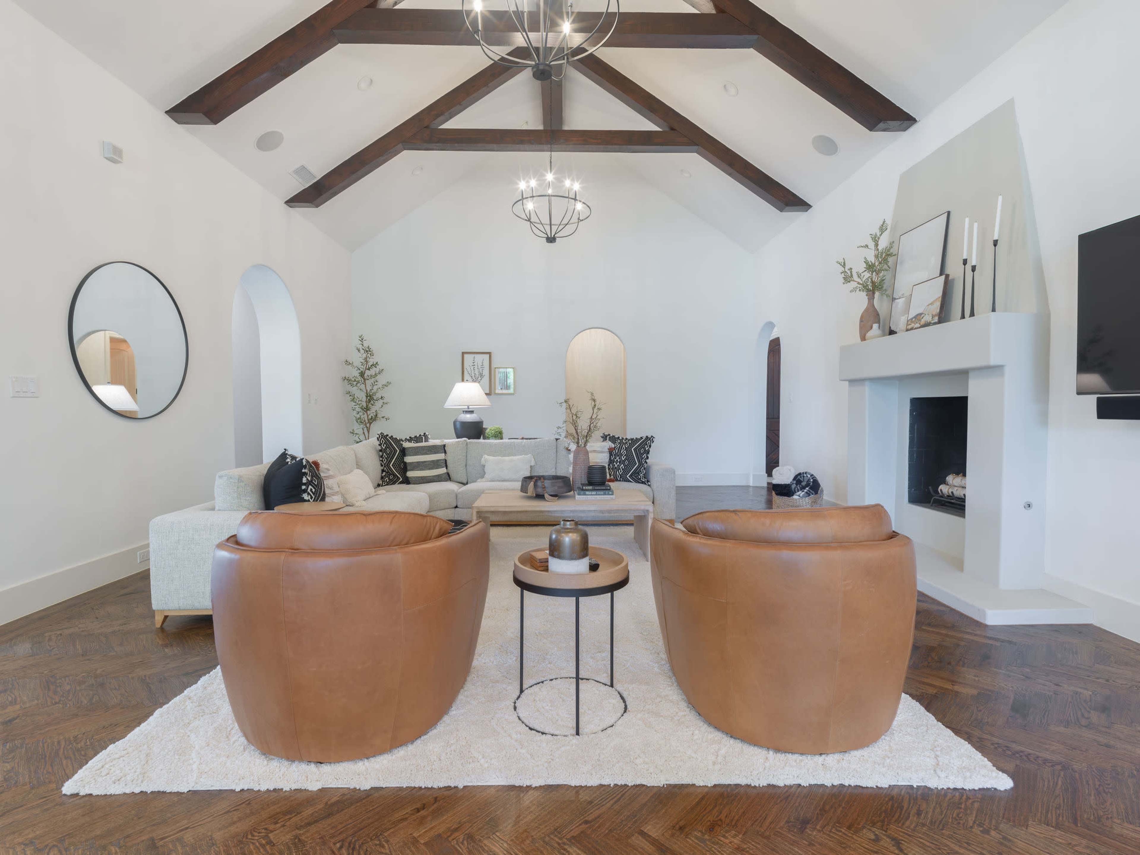 A spacious living room features two brown leather chairs facing a coffee table, with a light-colored sectional sofa and a fireplace in the background.