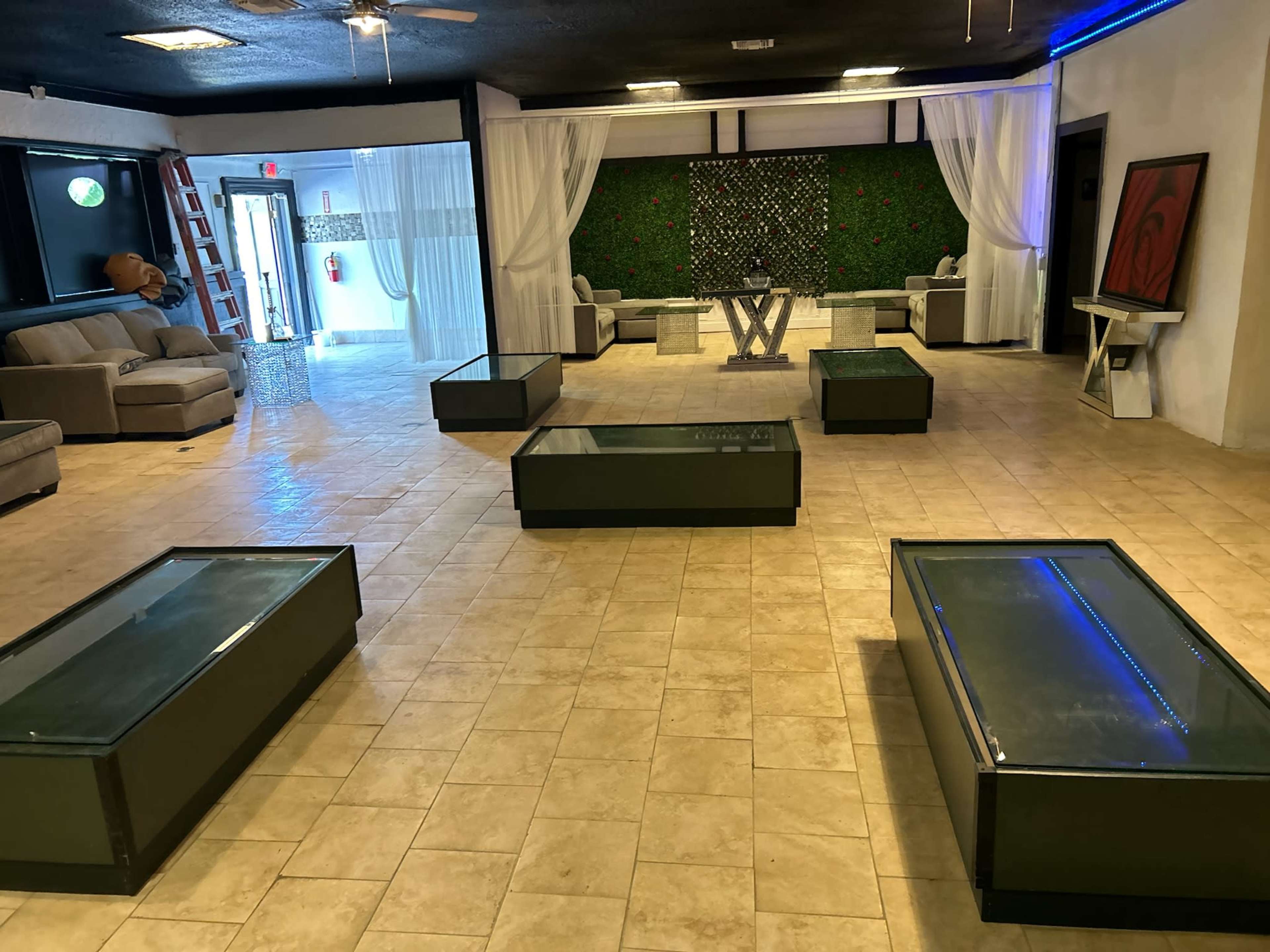 A spacious room with several glass-top coffee tables arranged on a tiled floor, flanked by sofas and decorative elements in a modern setting.