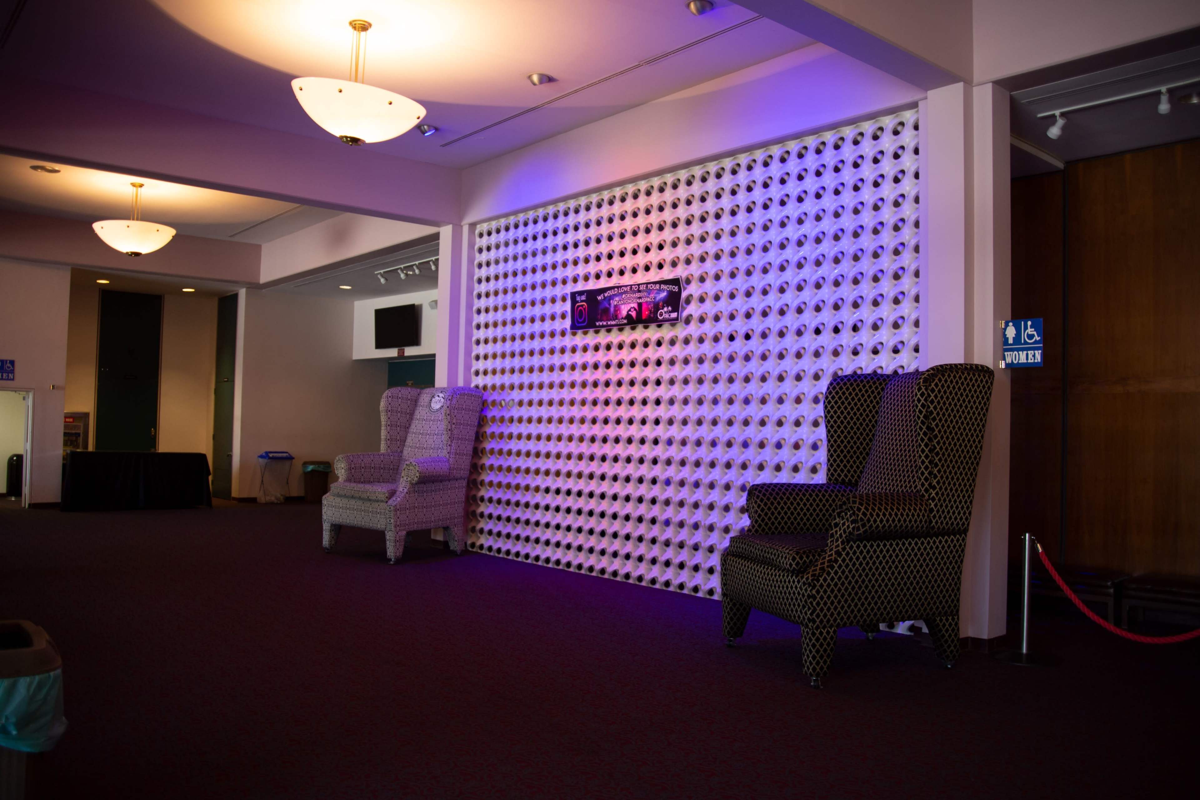 A spacious interior with two patterned armchairs facing a wall adorned with a textured design and a television mounted above.