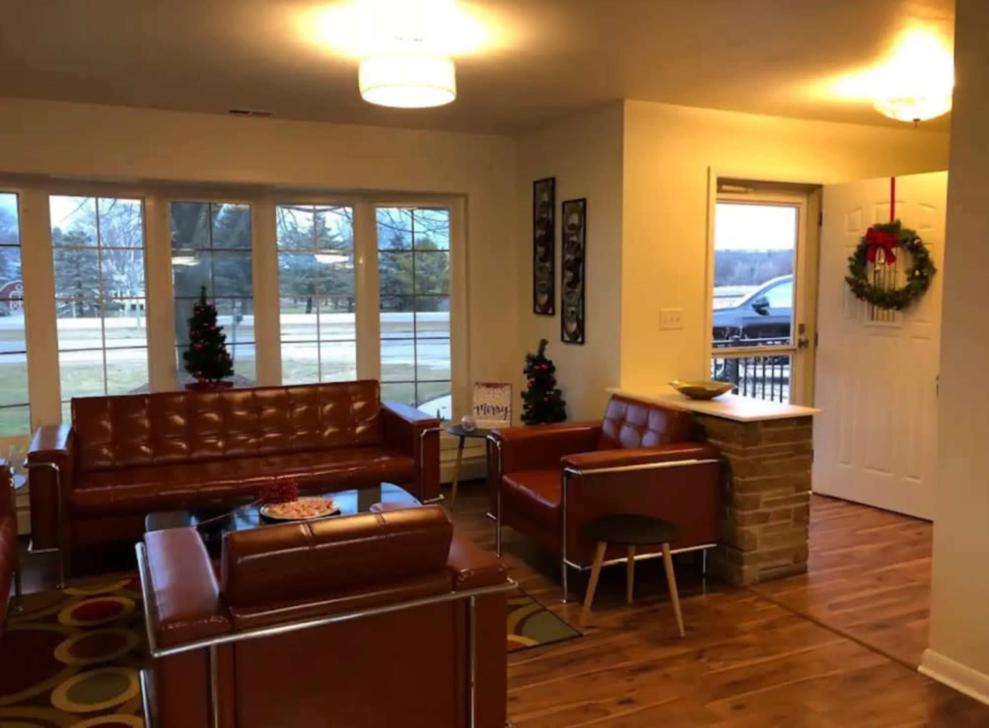 A living room with brown leather furniture, a coffee table, two small Christmas trees, and a door leading outside.