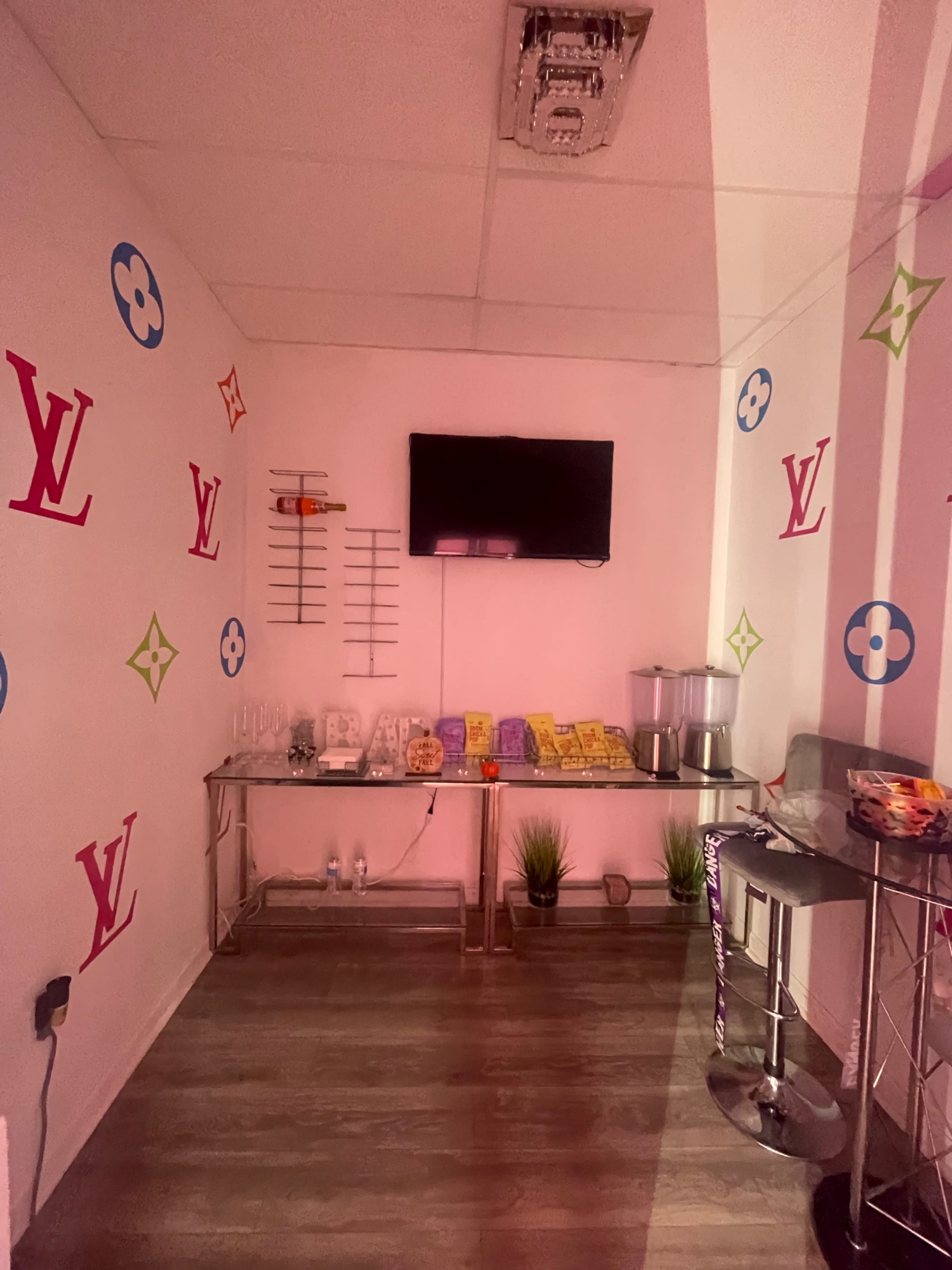 A small room decorated with Louis Vuitton logos, featuring a television on the wall, a table with various items, and modern bar stools.