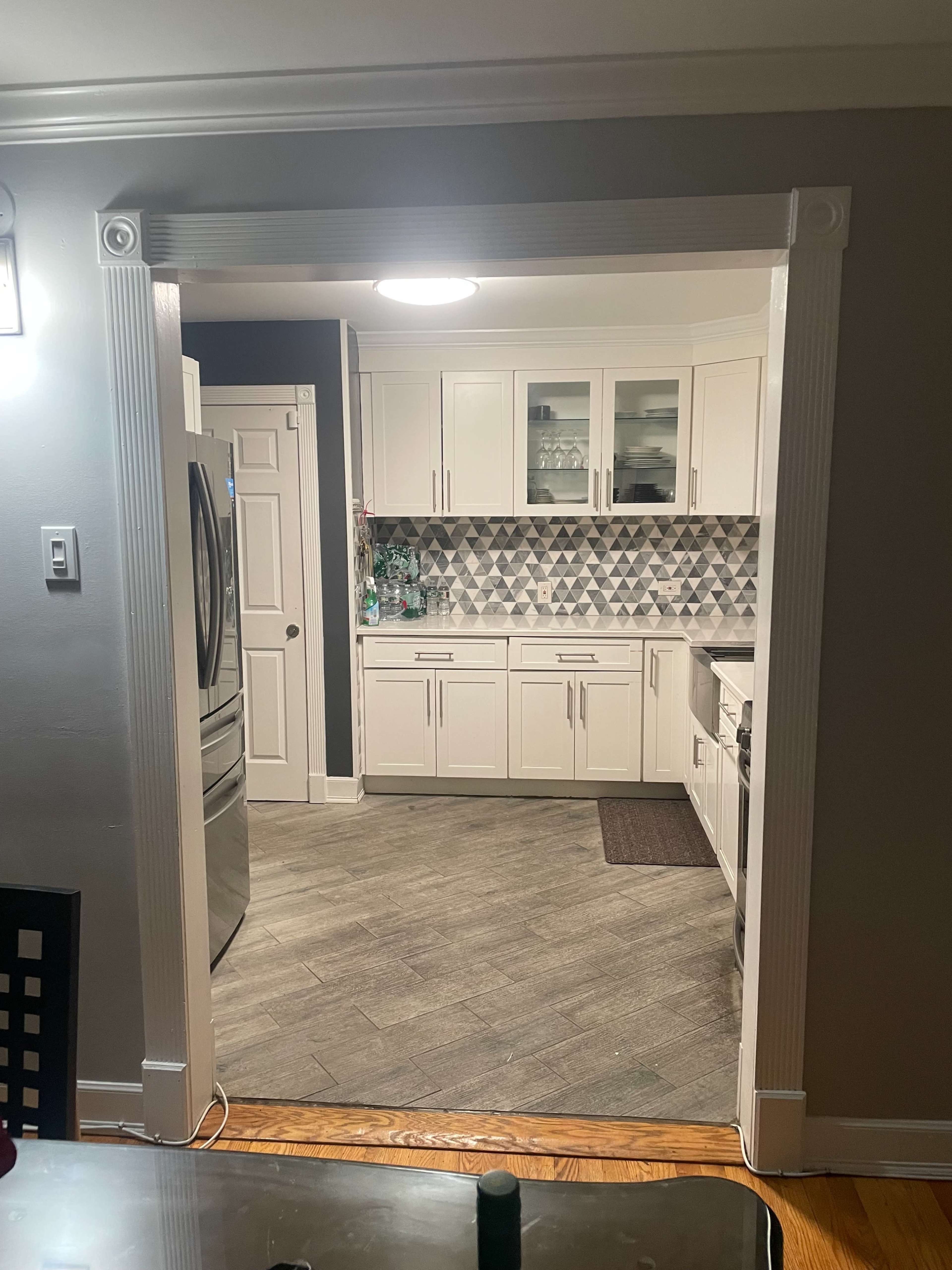The image shows a kitchen with white cabinets and a patterned backsplash, viewed through an open archway in a nearby dining area.