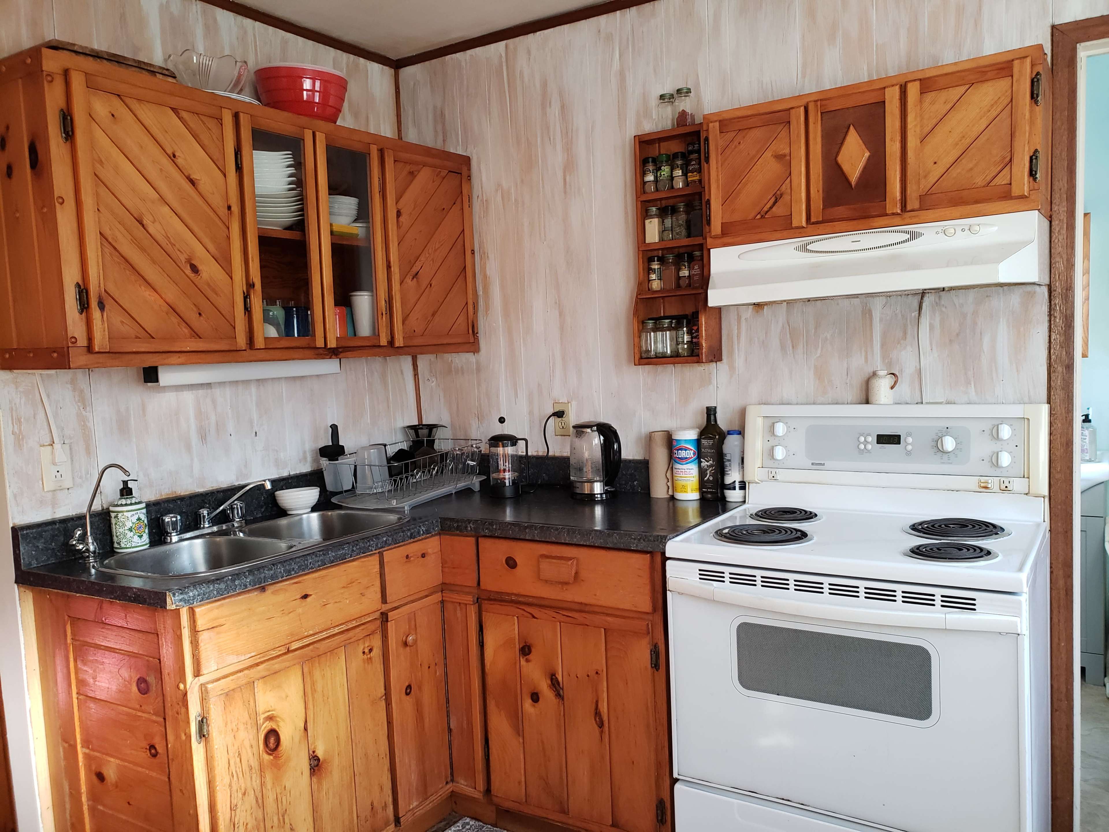 A wooden kitchen featuring an oven, a sink, and upper cabinets filled with dishware and spices.