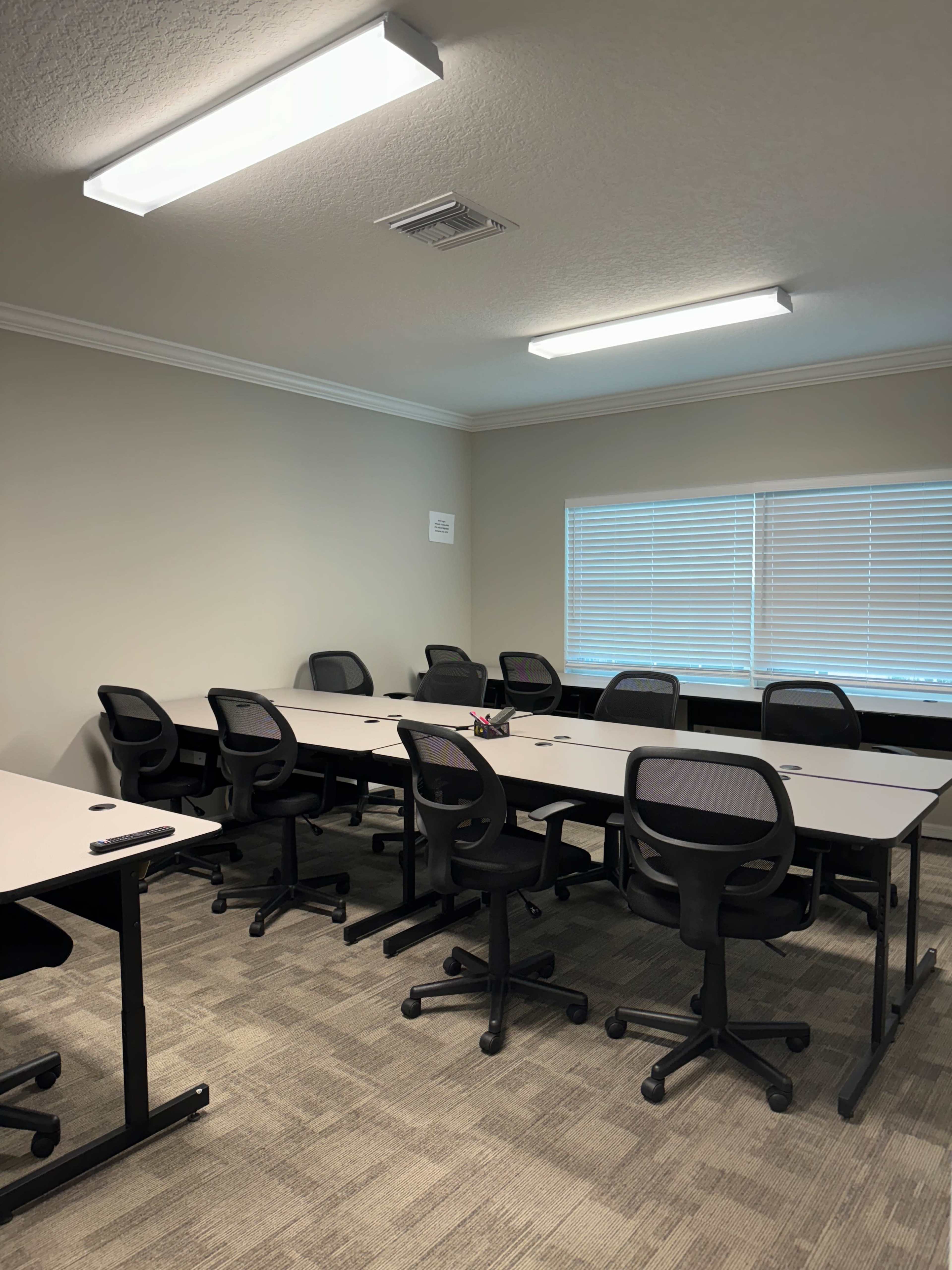 A light-colored meeting room with several empty desks and ergonomic chairs arranged around them.