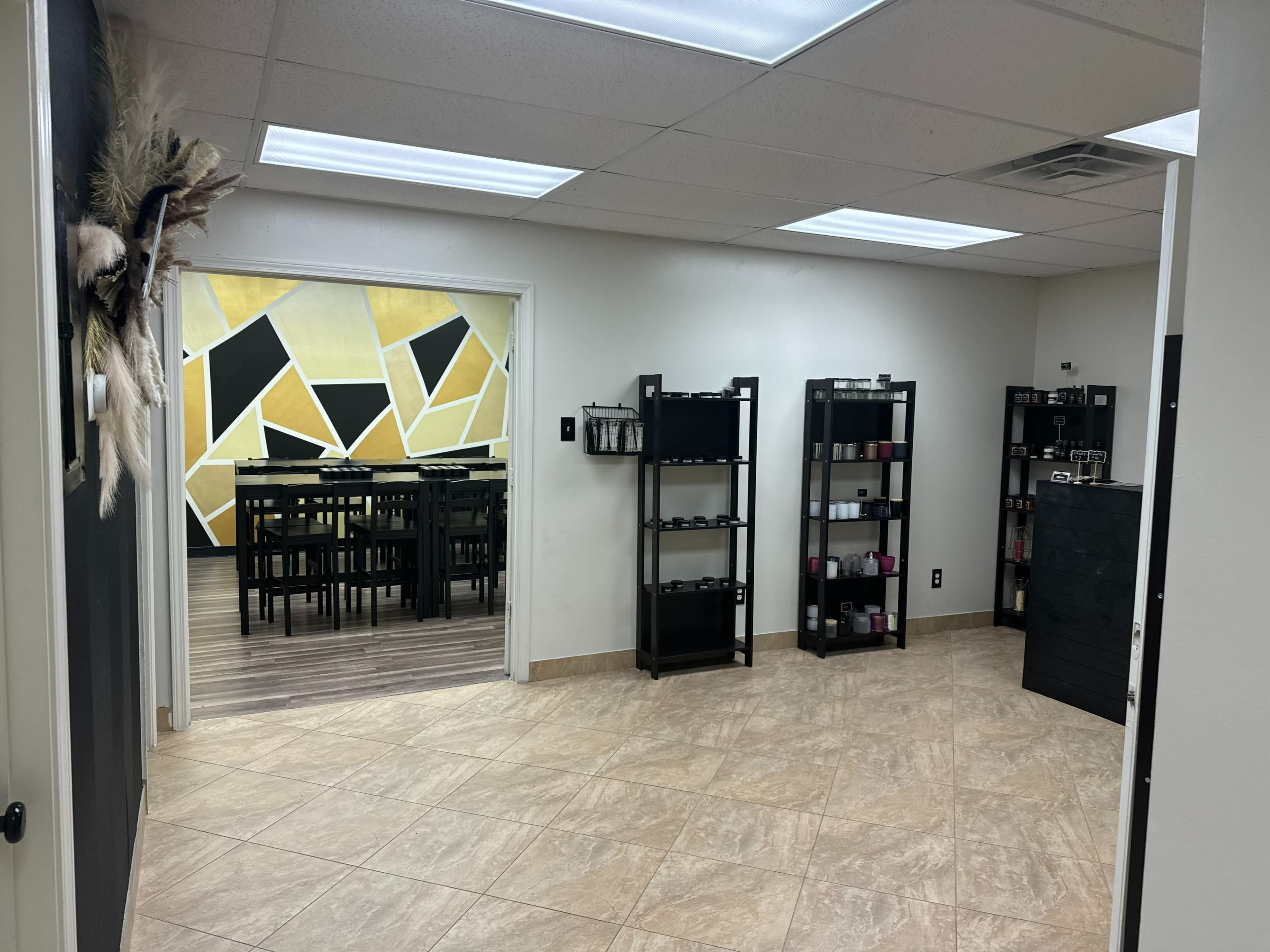 A well-lit room with tile flooring, featuring shelves with products on the right and an adjoining area with a large table and chairs in the background.