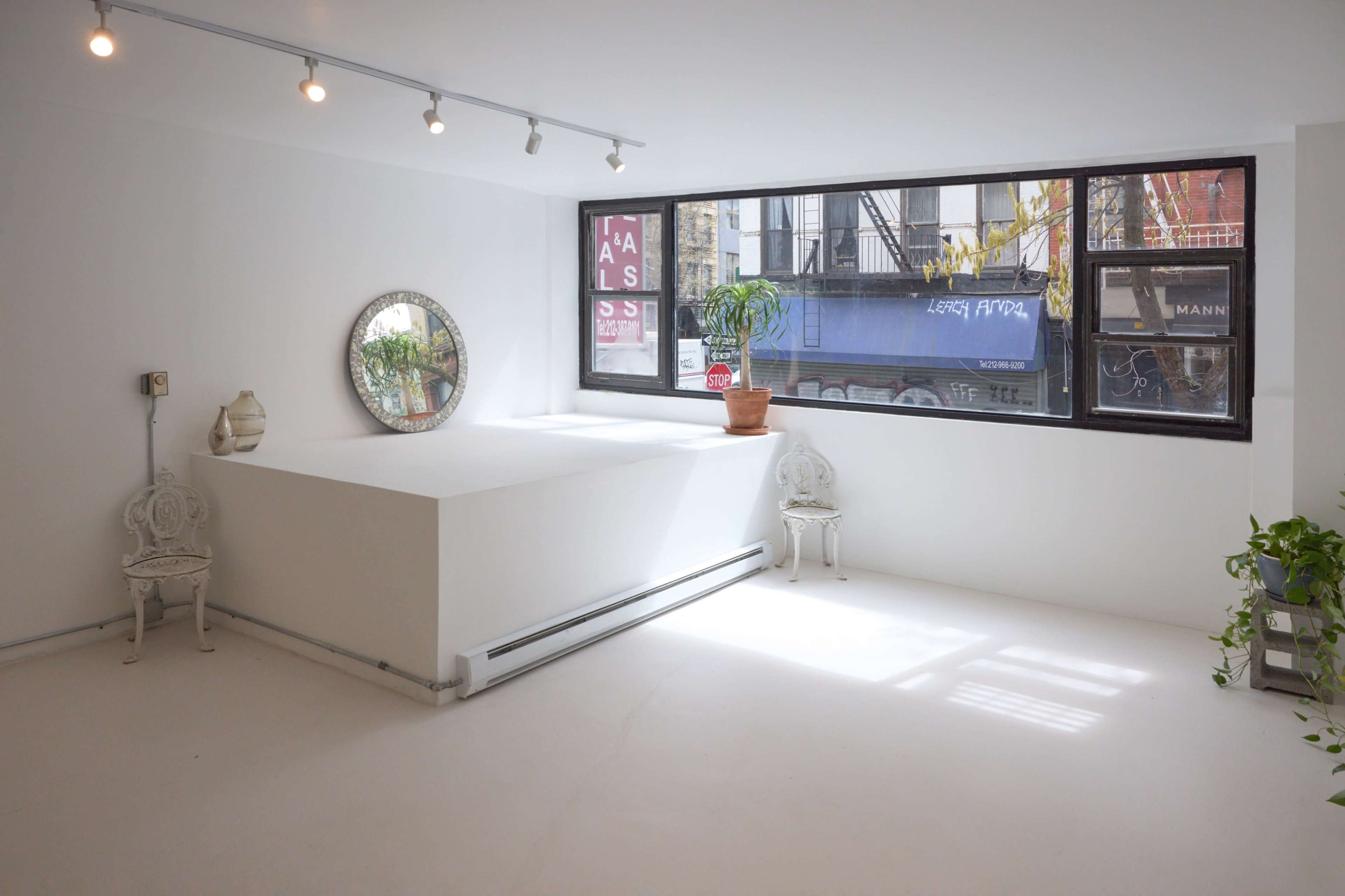 A minimalistic, bright room with large windows, featuring a mirror, potted plants, and two white chairs.