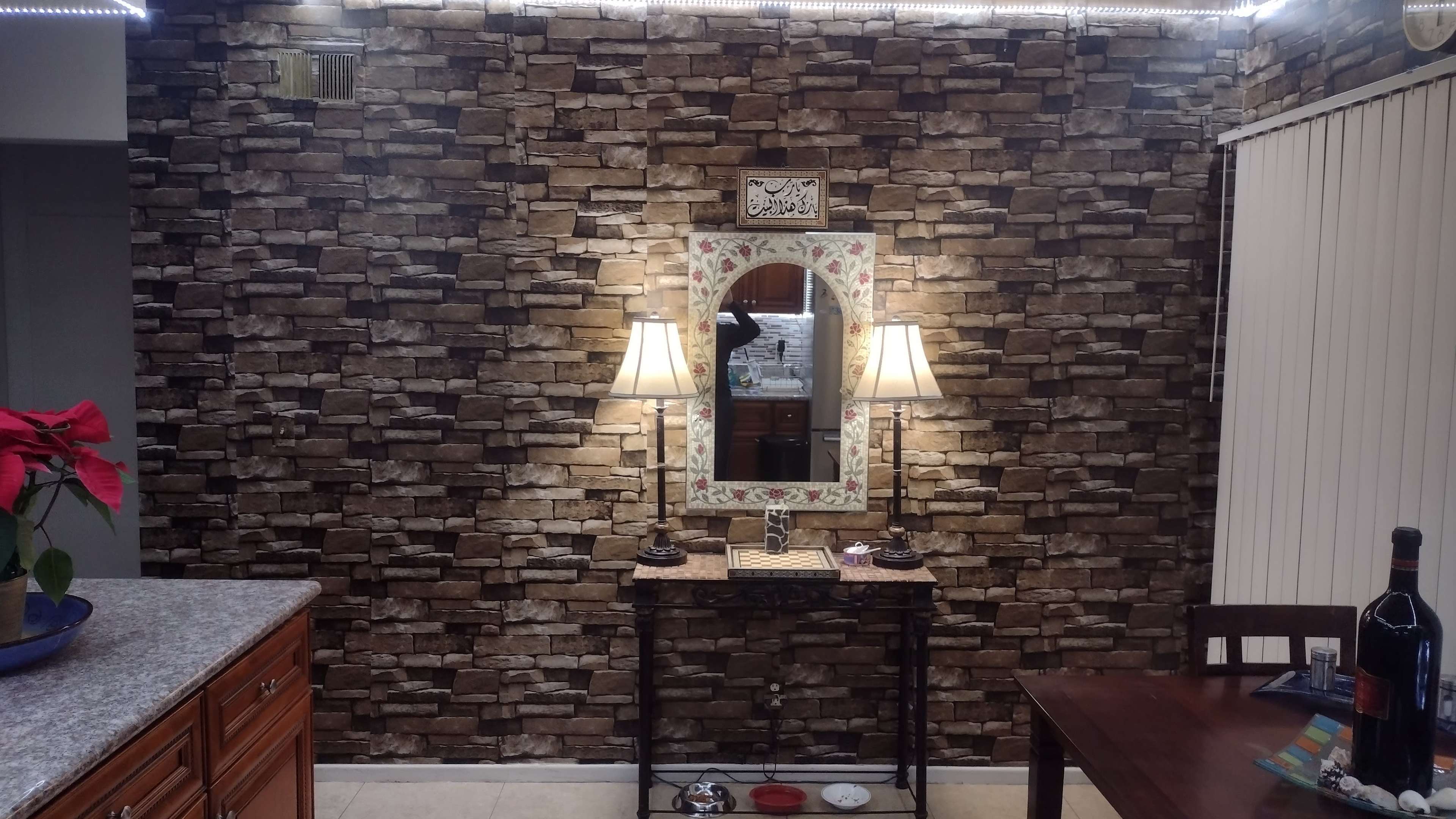 A rustic stone wall with a mirror framed in floral designs, flanked by two table lamps on a narrow console table.