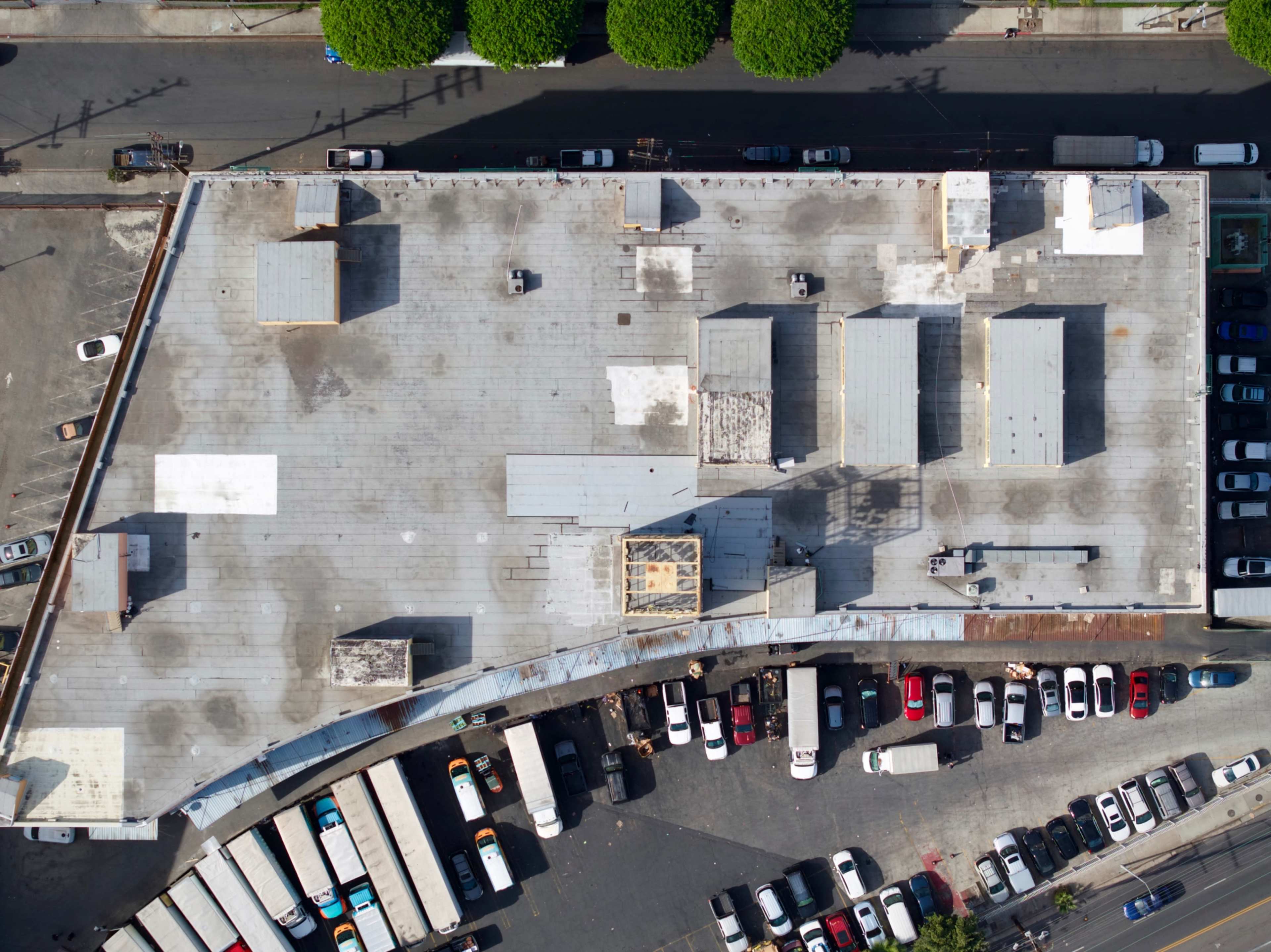 An aerial view shows a large, flat-roofed building surrounded by parked vehicles and tree-lined streets.