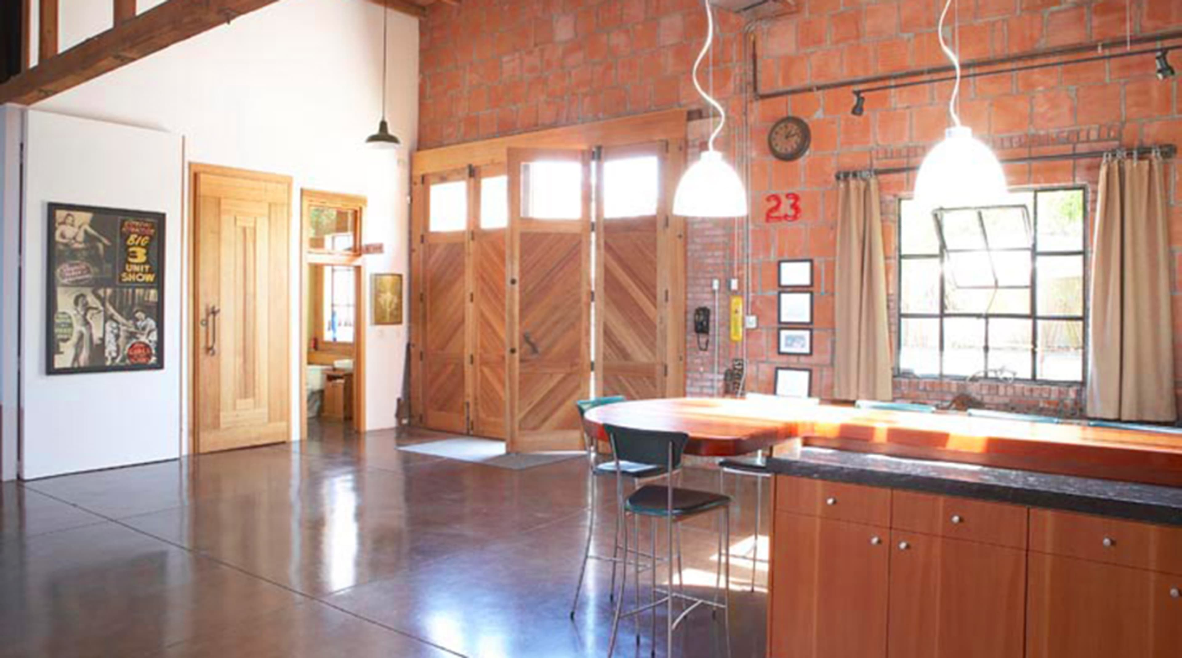 An open-concept industrial-style interior with a wooden kitchen island, brick walls, and large windows.