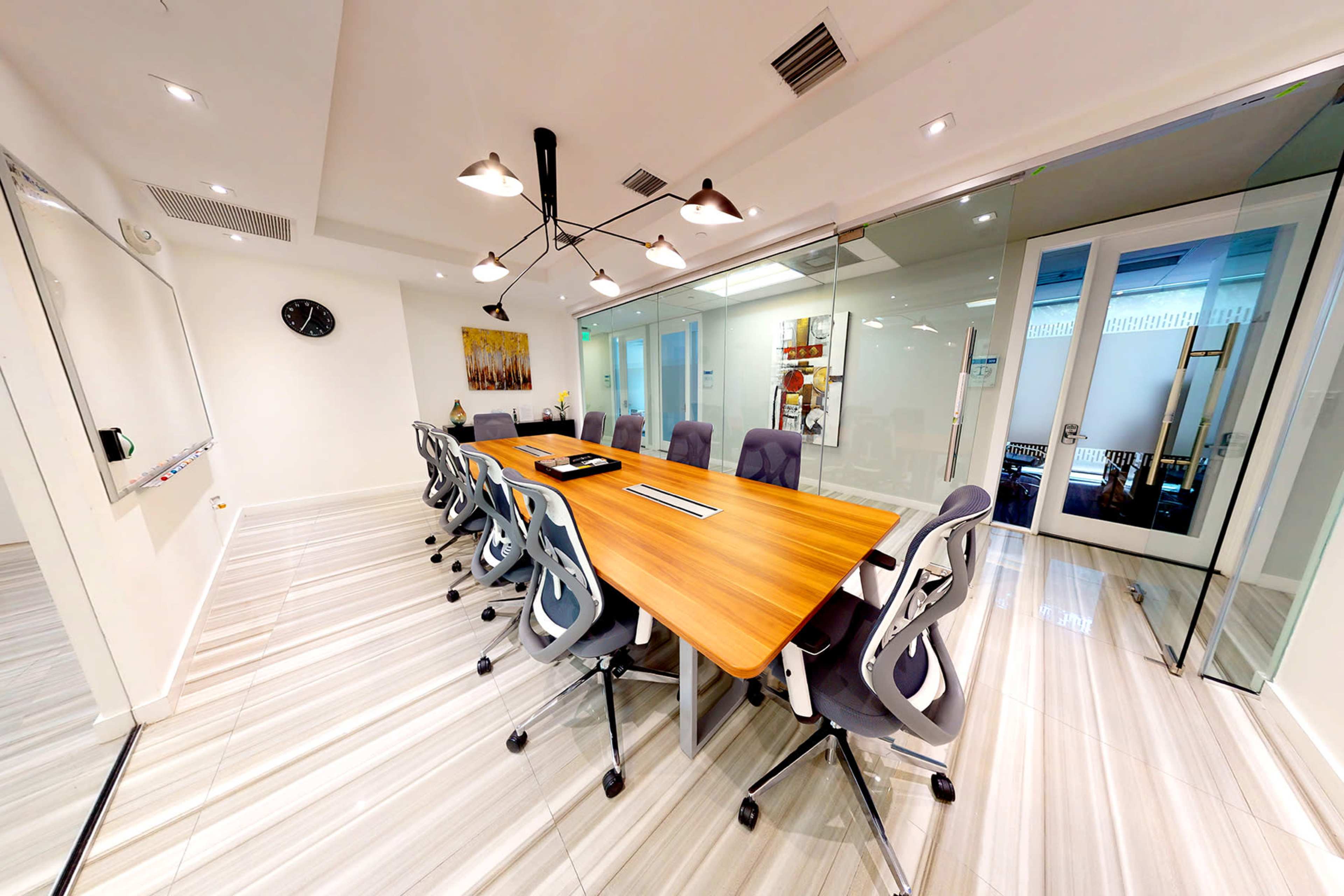 The image shows a modern conference room with a large wooden table surrounded by ergonomic chairs, glass walls, and contemporary lighting fixtures.