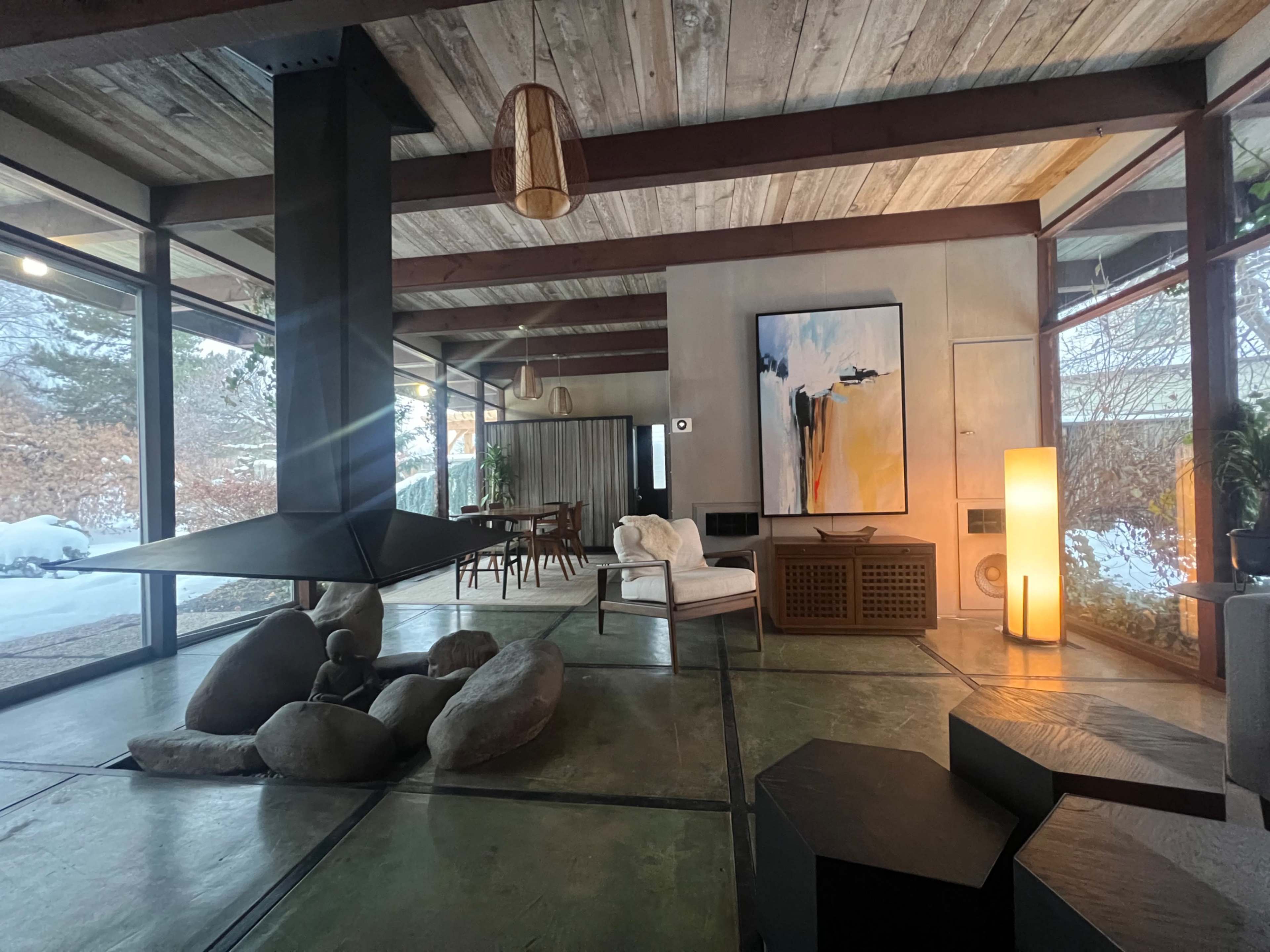 A spacious living area features a central stone arrangement, a modern fireplace, and large windows providing a view of the snowy outdoors.