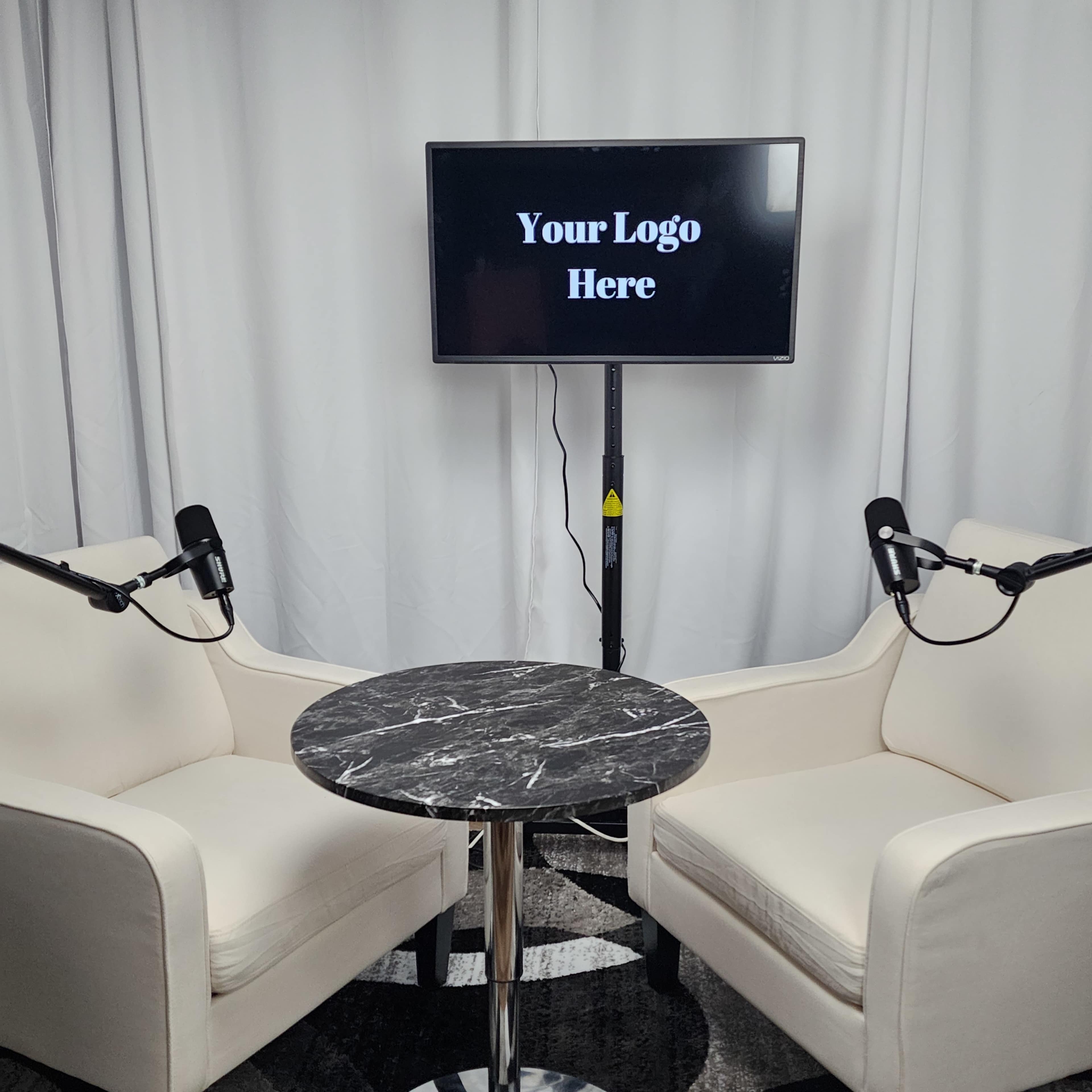 Two white chairs positioned around a round black marble table, with a monitor displaying "Your Logo Here" in the background.