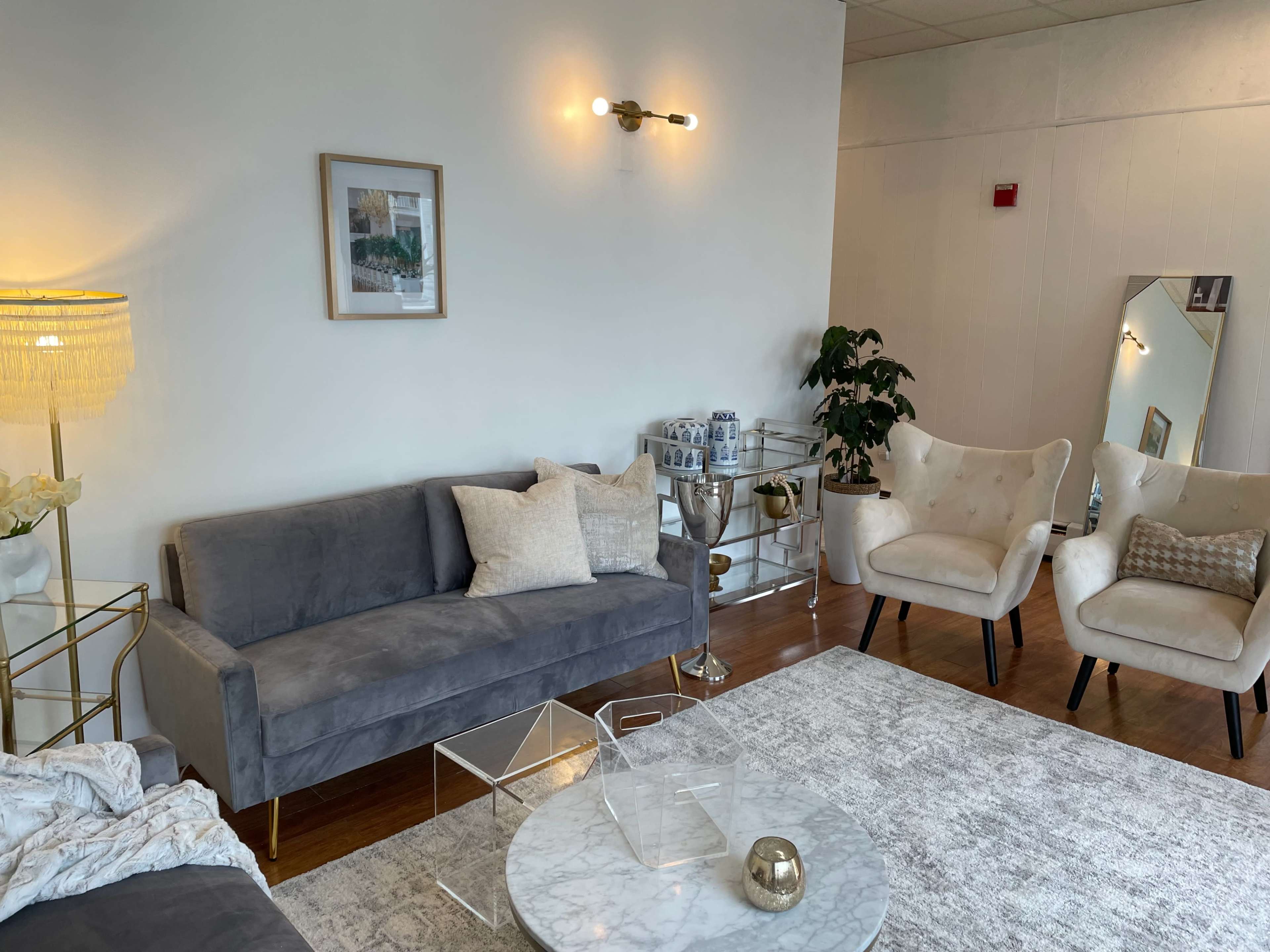 A modern living room features a gray sofa, two white armchairs, a marble coffee table, and a decorative lamp, all arranged on a light area rug.