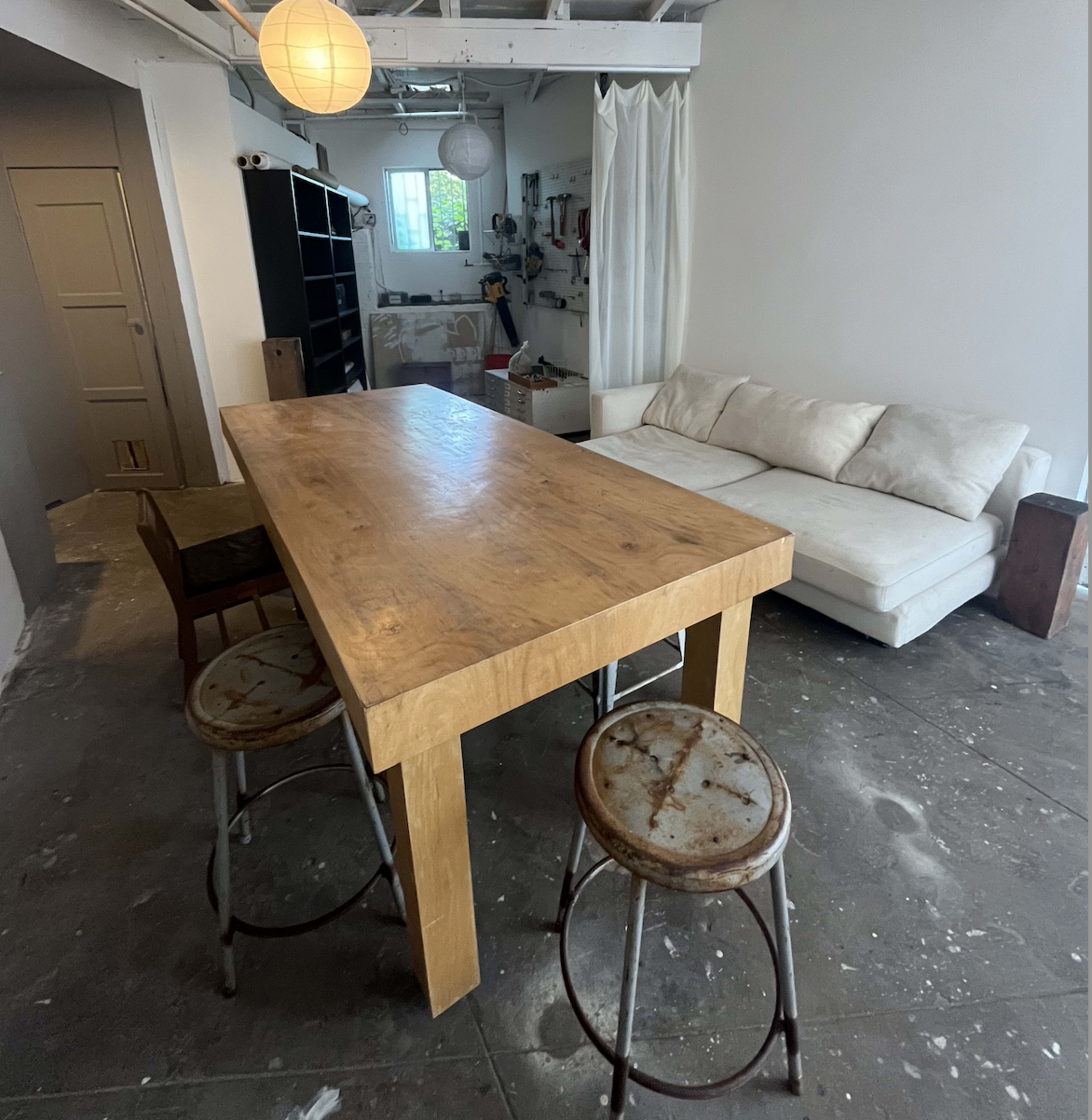 A spacious room featuring a wooden dining table surrounded by three metal stools, with a white sectional sofa positioned against the wall.