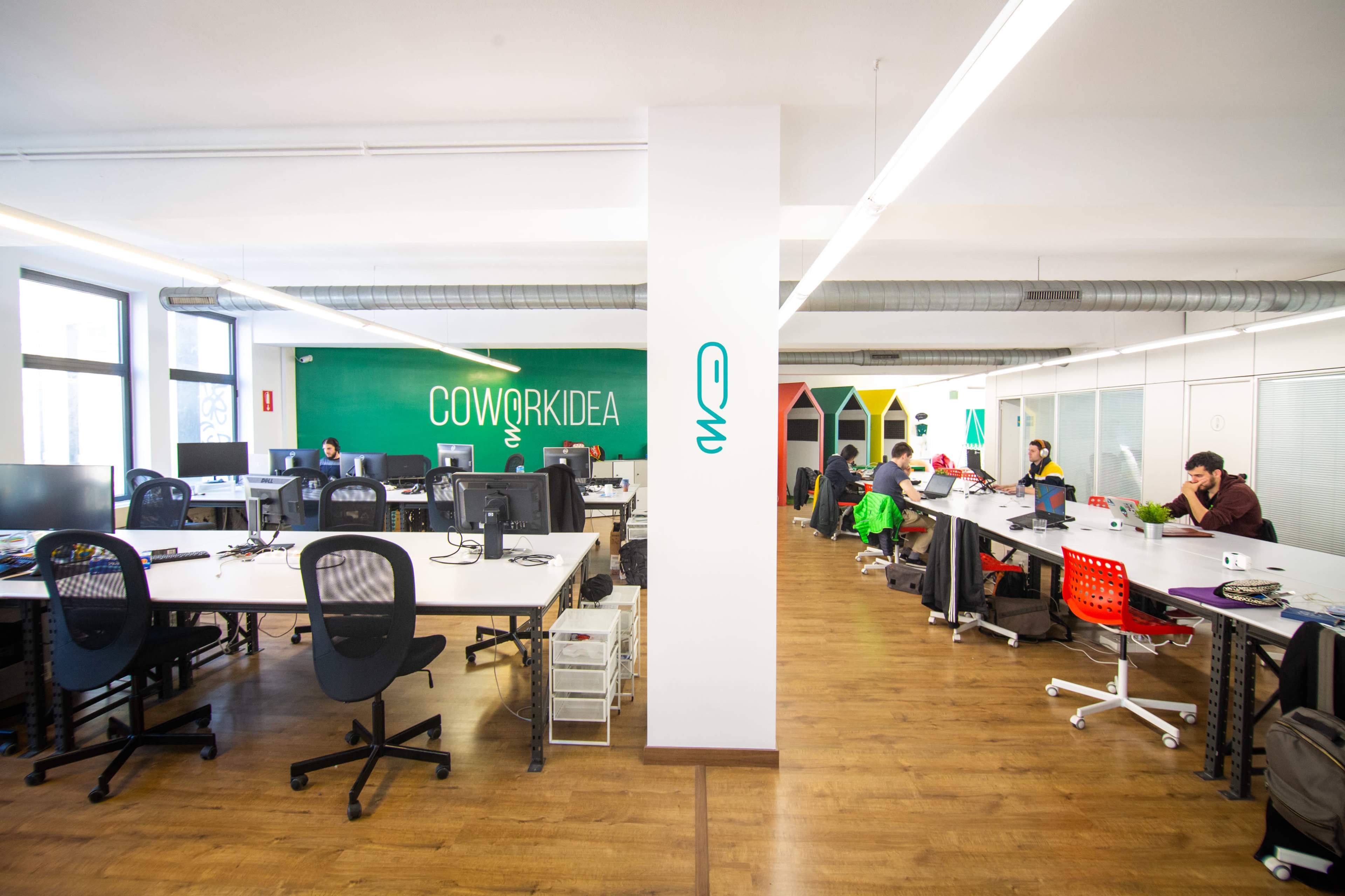 A modern co-working space with several people working at desks, featuring a green accent wall that reads "COWORKIDEA."