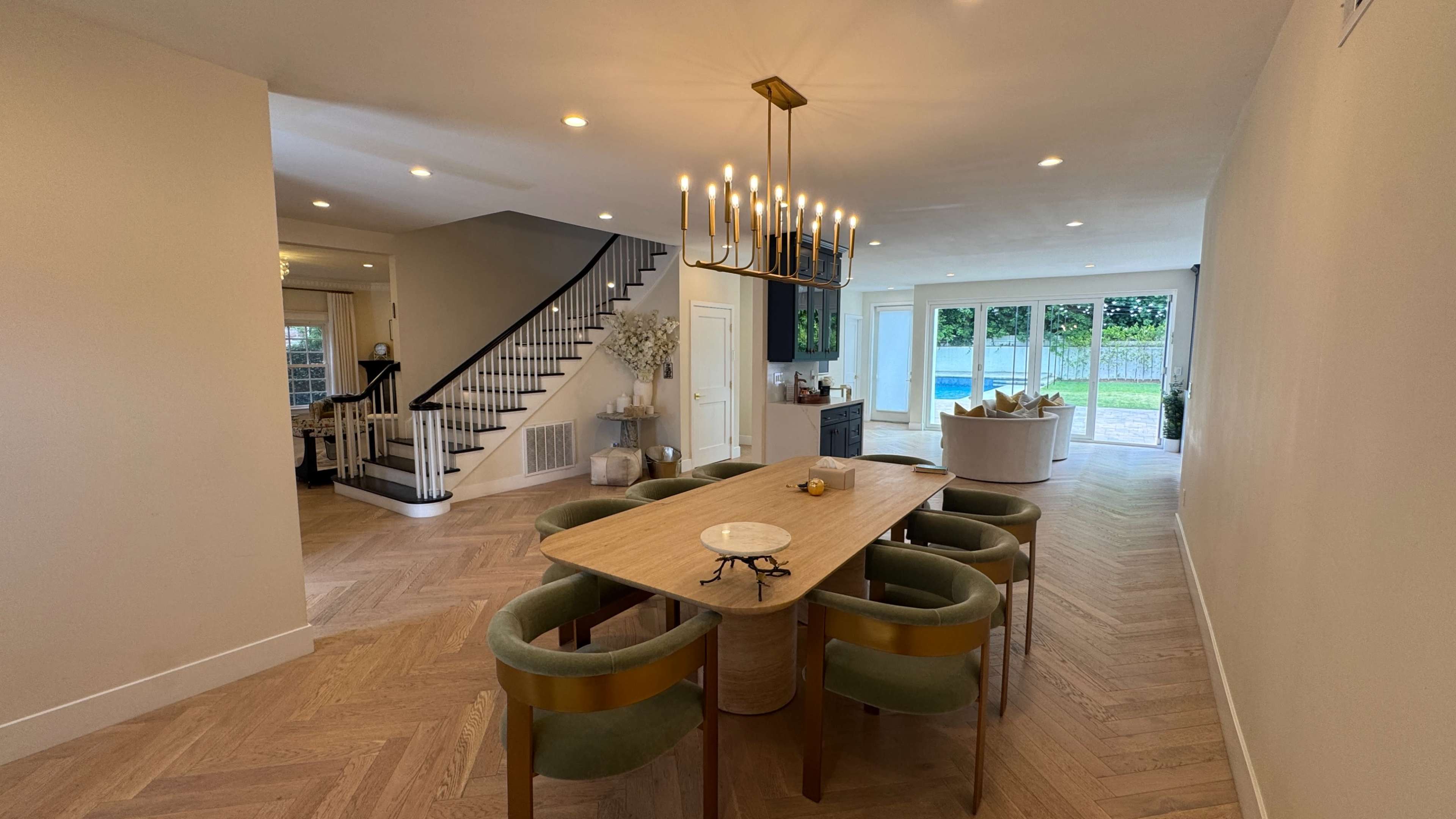 The image shows a spacious dining area with a wooden table and green chairs, leading to a porch with large glass doors that open to an outdoor space.