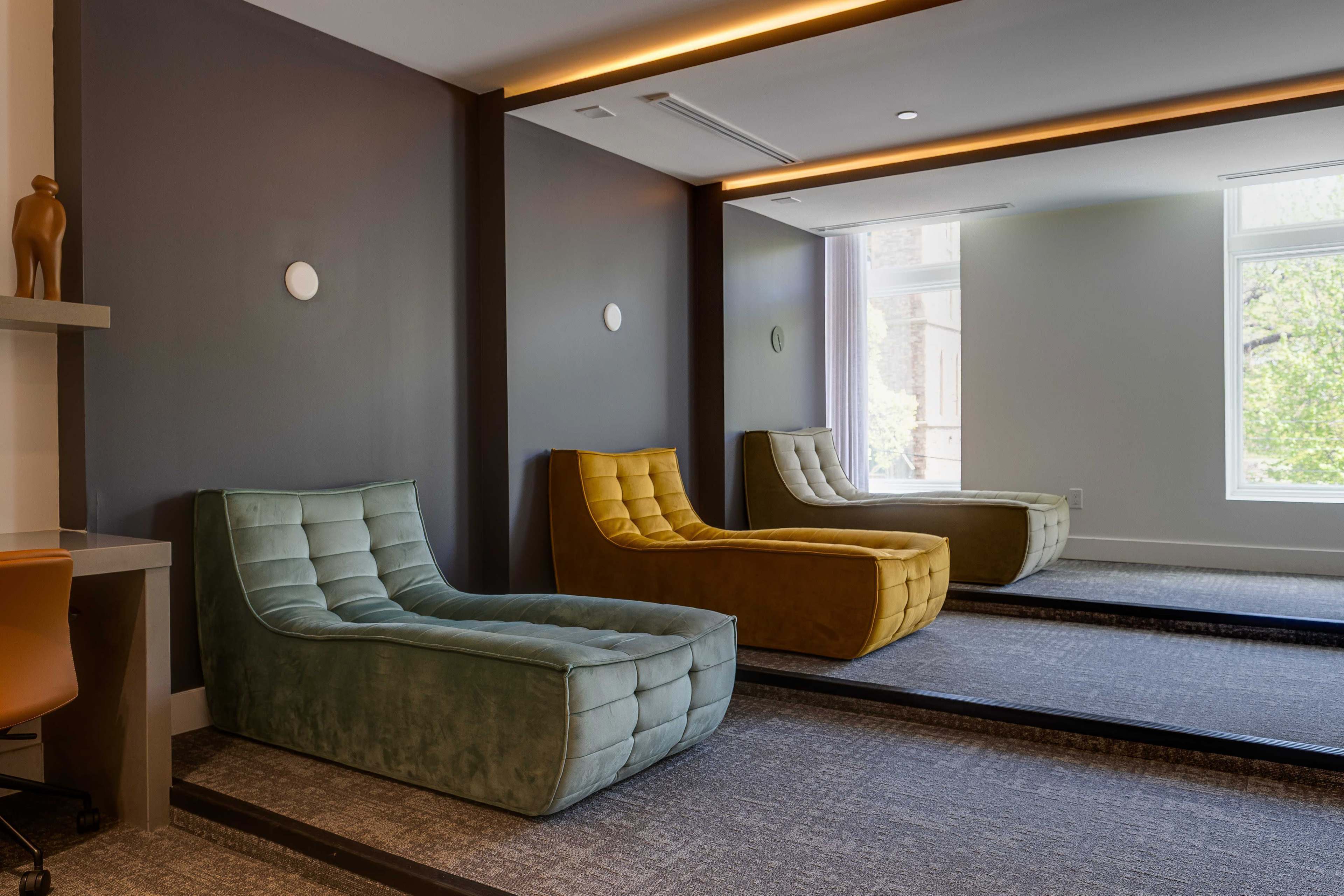 The image shows three lounge chairs in different colors positioned in a modern room with a mirrored wall.