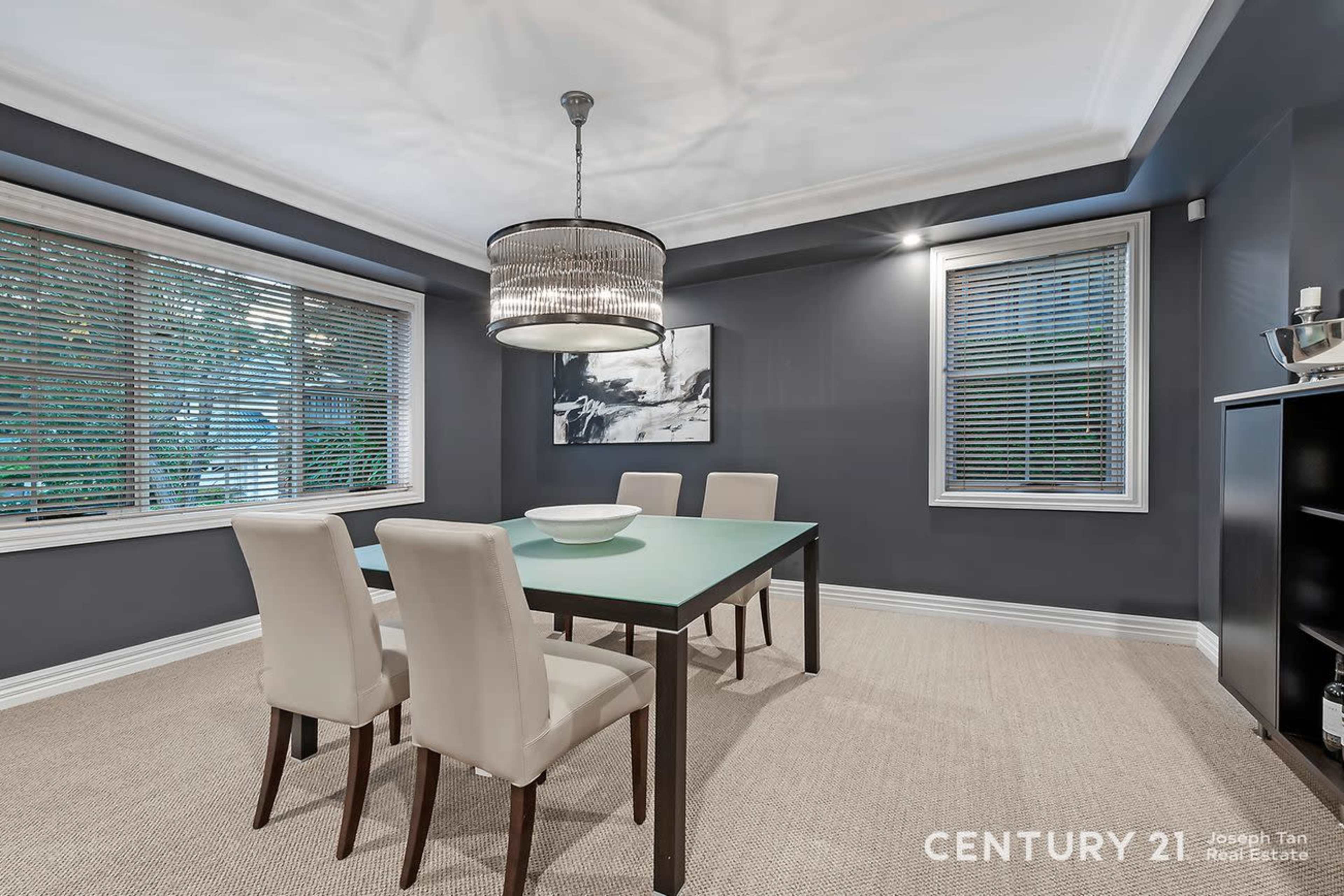 The image shows a modern dining room with a rectangular table surrounded by four upholstered chairs, a decorative pendant light, and dark gray walls.