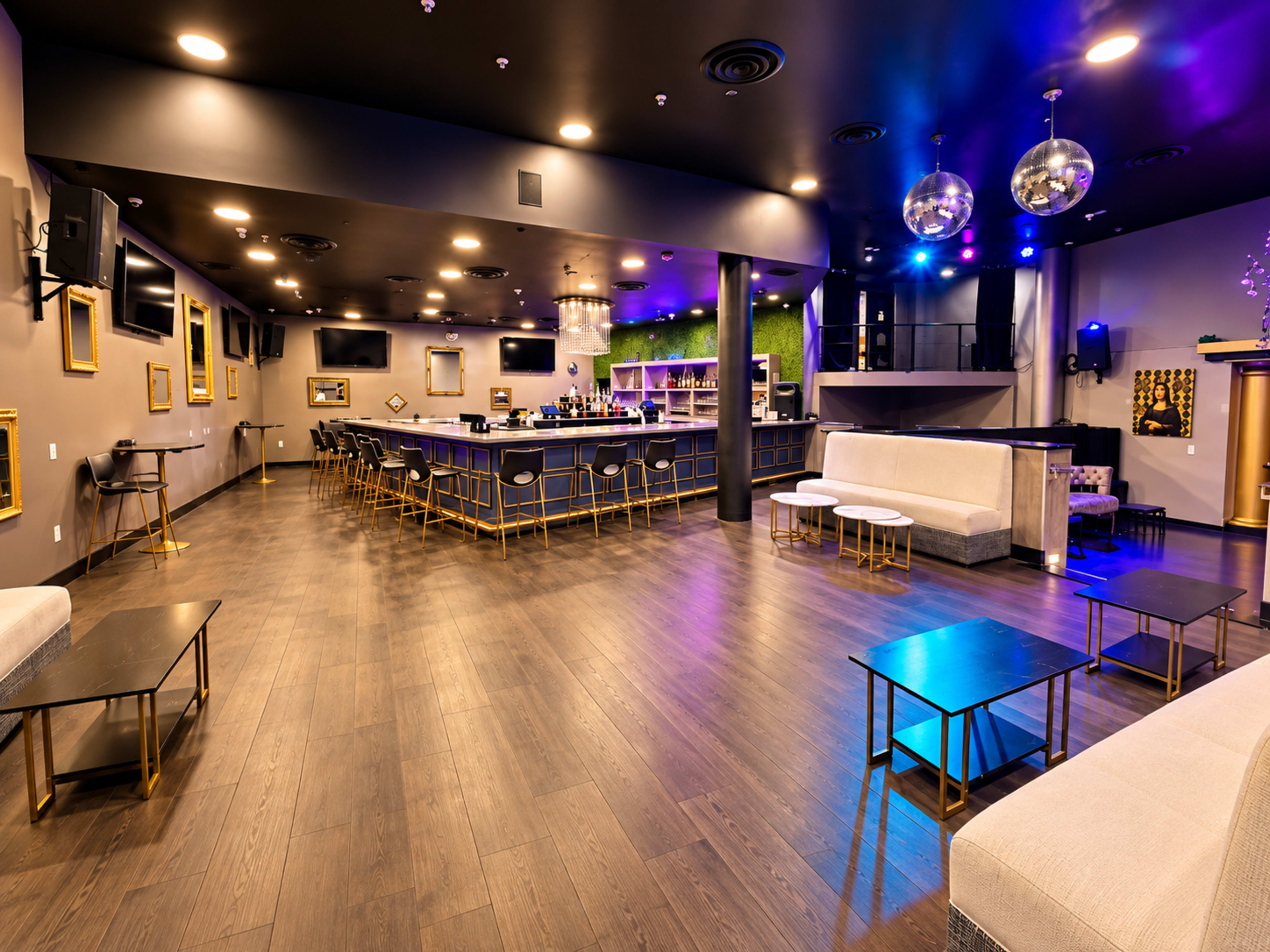 The image shows a modern bar interior with a sleek design, featuring a long bar counter, seating areas, and decorative lighting.