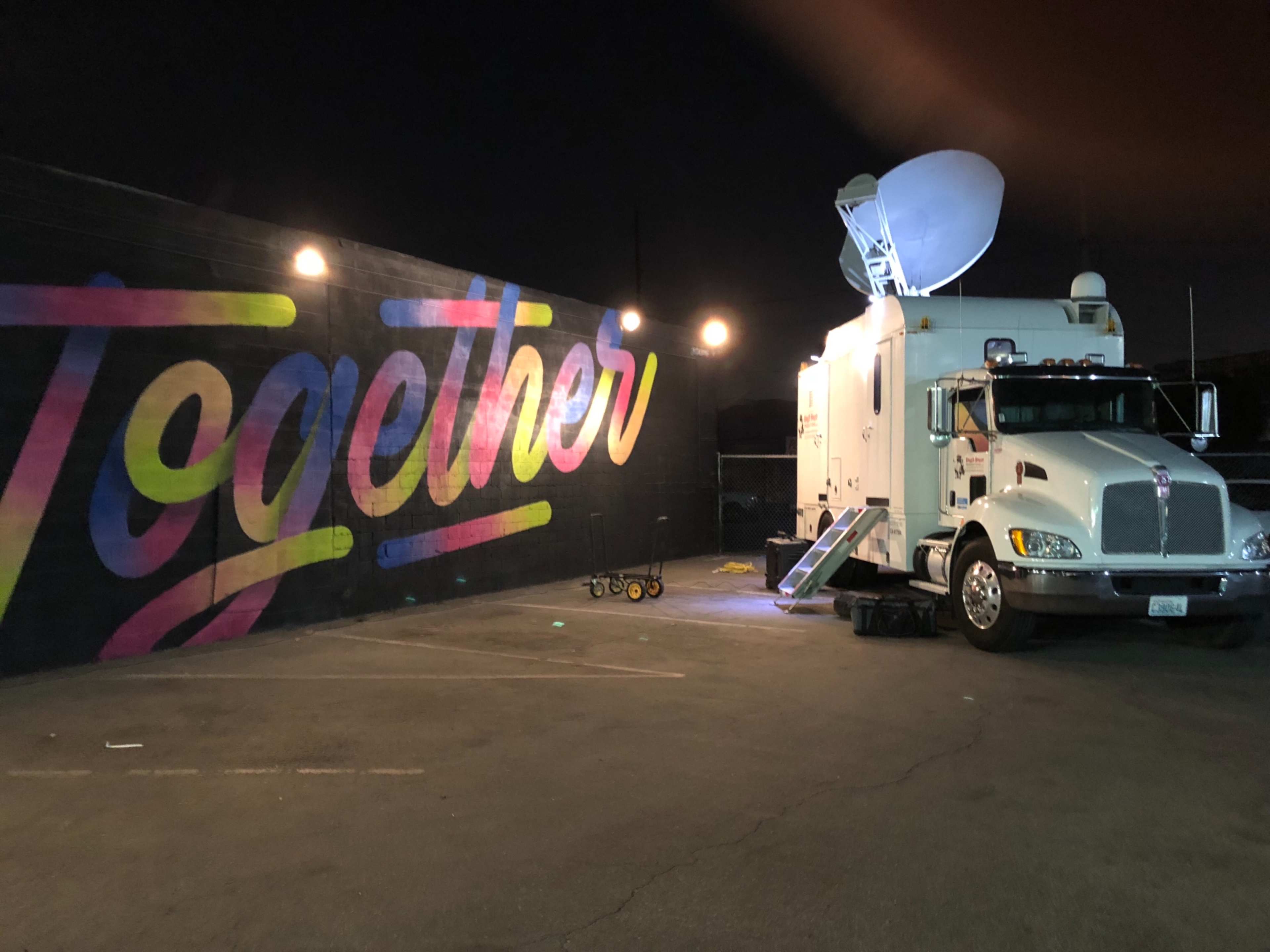 A satellite truck is parked next to a brightly colored mural that spells out "Together."