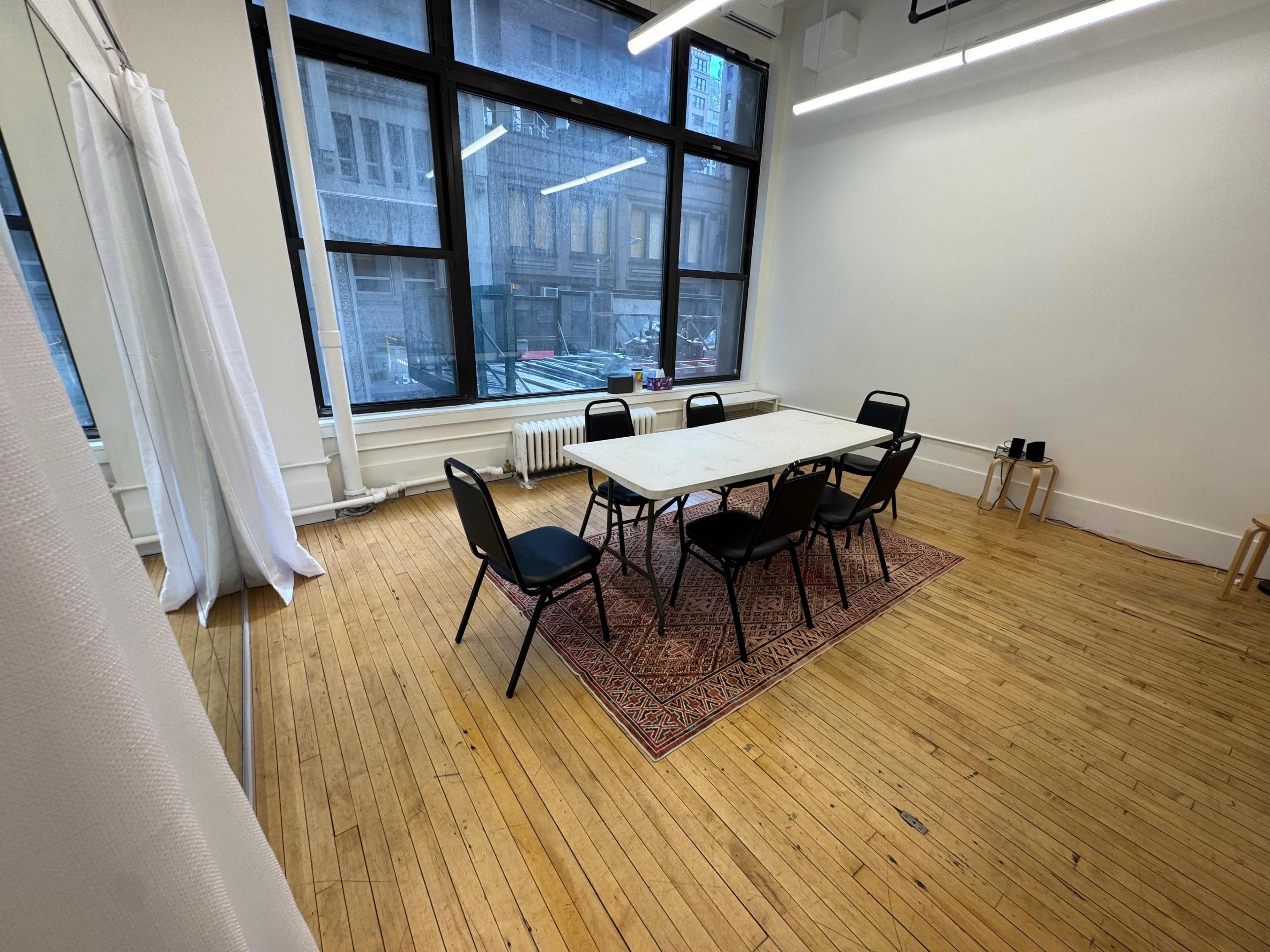 A rectangular table is surrounded by six chairs in a bright, spacious room with large windows.