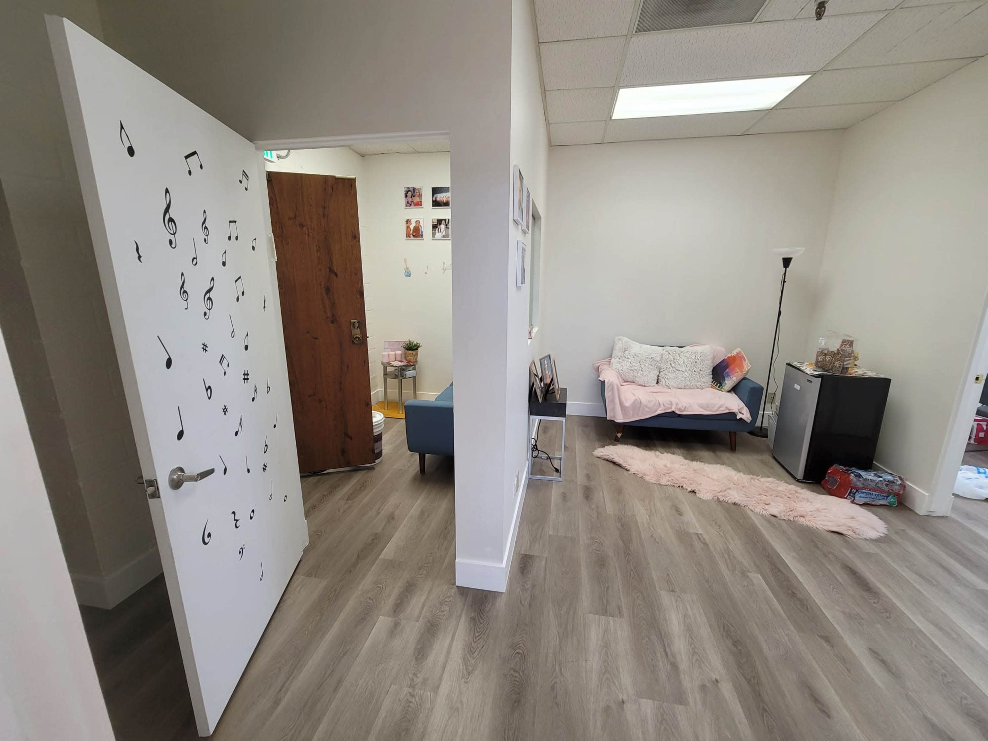 A room with a doorway featuring music notes, a pink couch, a lamp, and a small fridge against the wall.