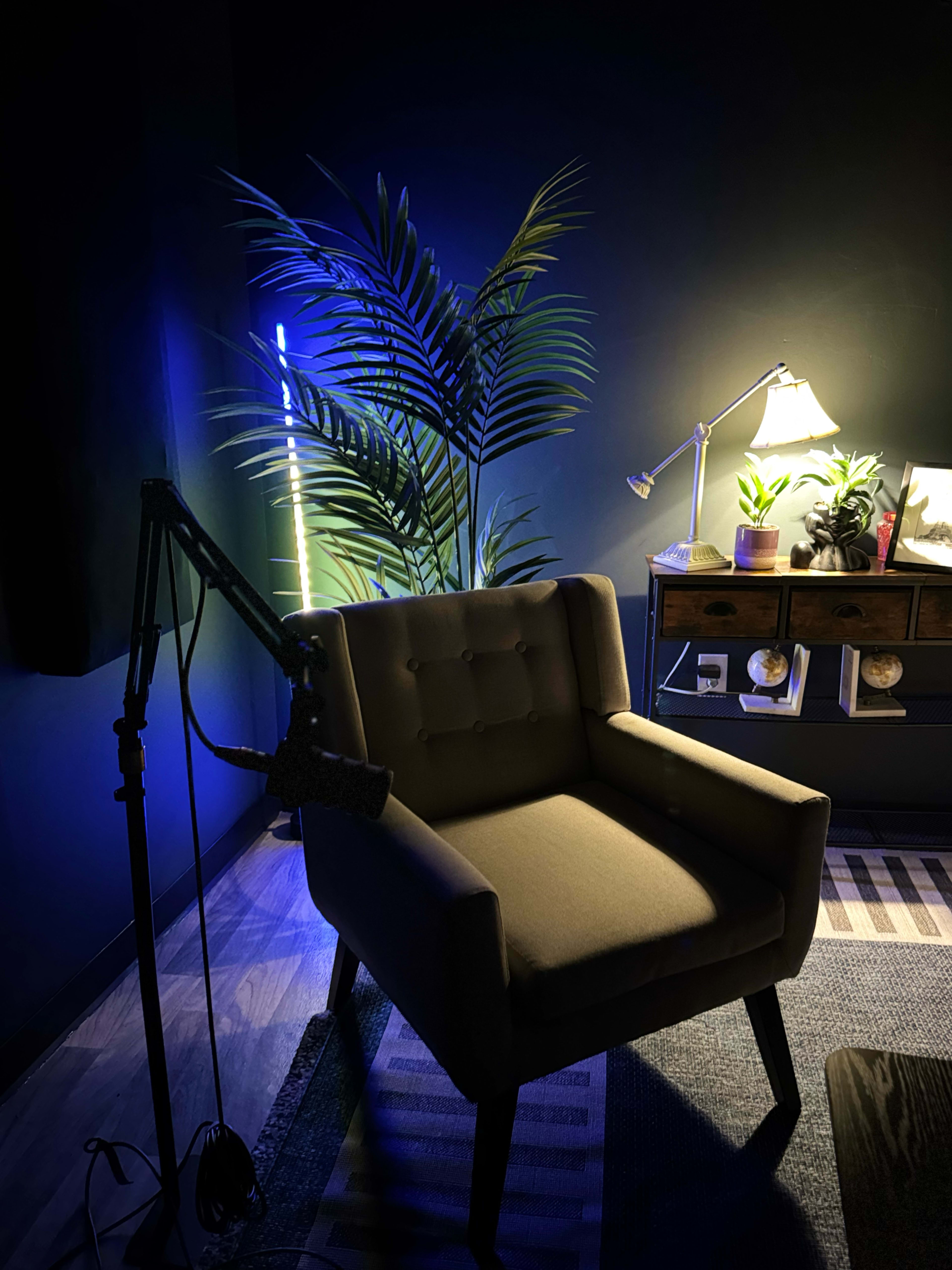 The image shows a cozy room featuring a brown armchair beside a desk with plants and a lamp, illuminated by soft blue lighting.