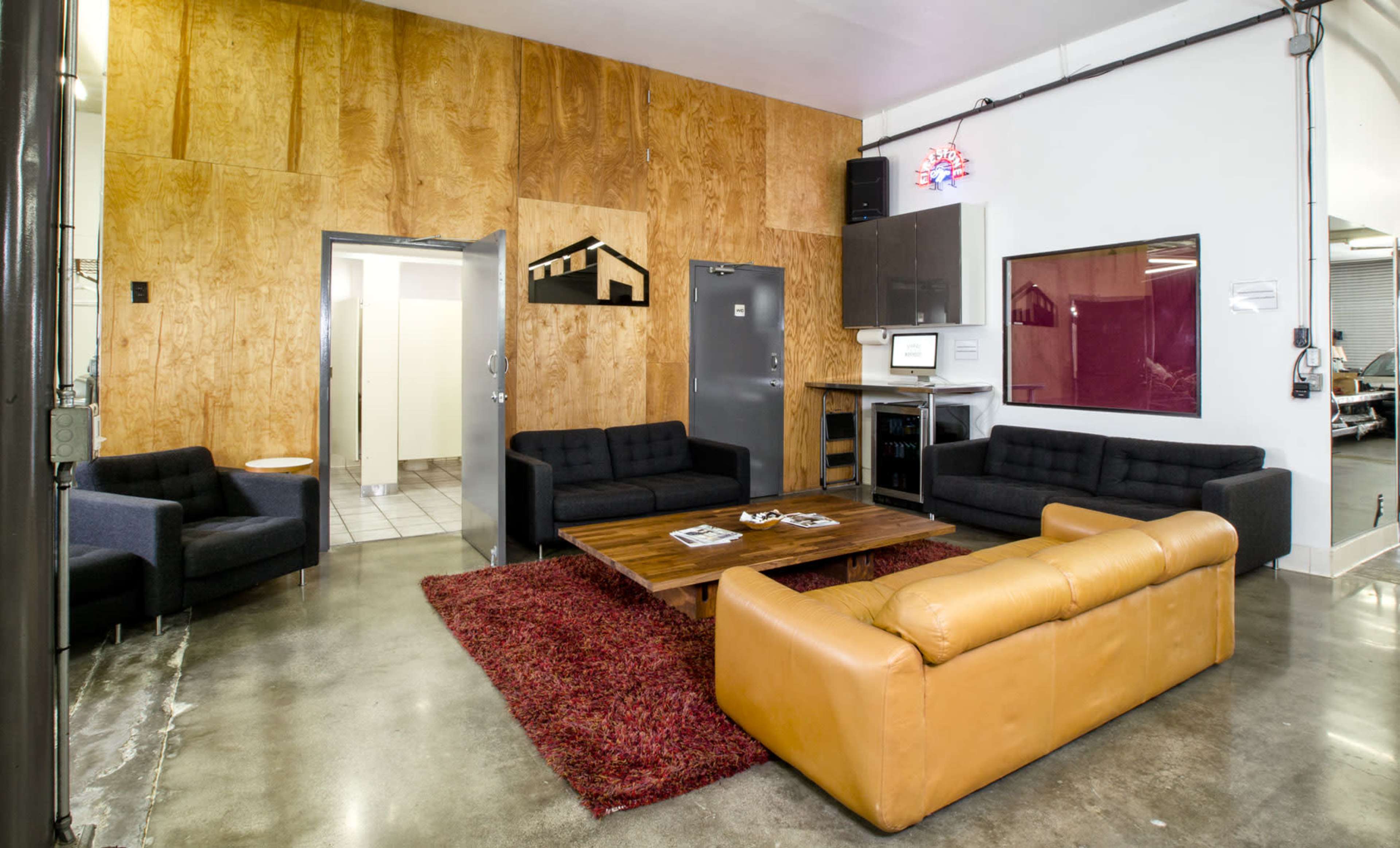 The image shows a modern lounge area with dark sofas, a brown leather couch, a wooden wall, and a coffee table on a red carpet.