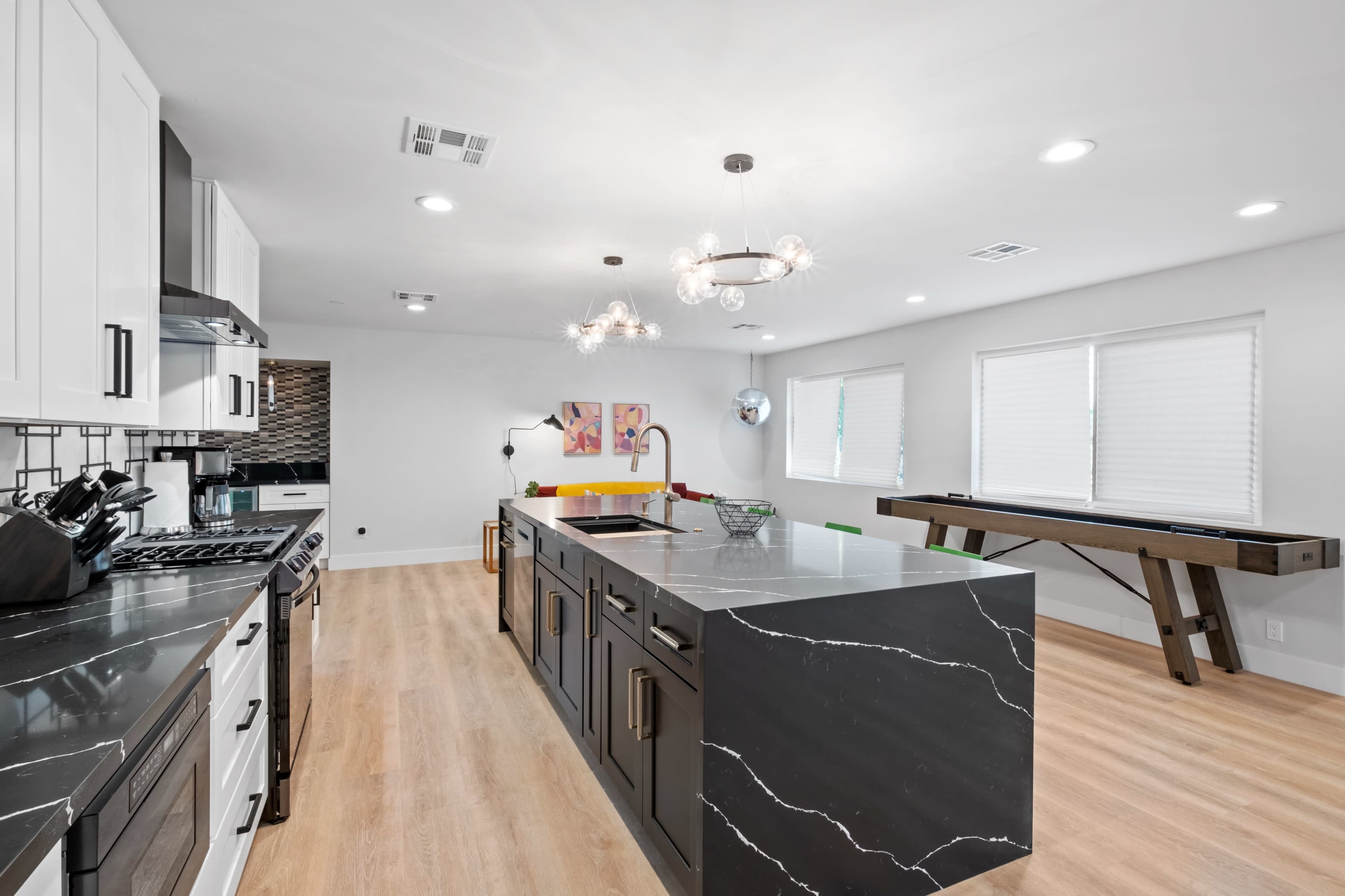 A modern kitchen featuring a large black marble island, stainless steel appliances, and a light-colored wooden floor.