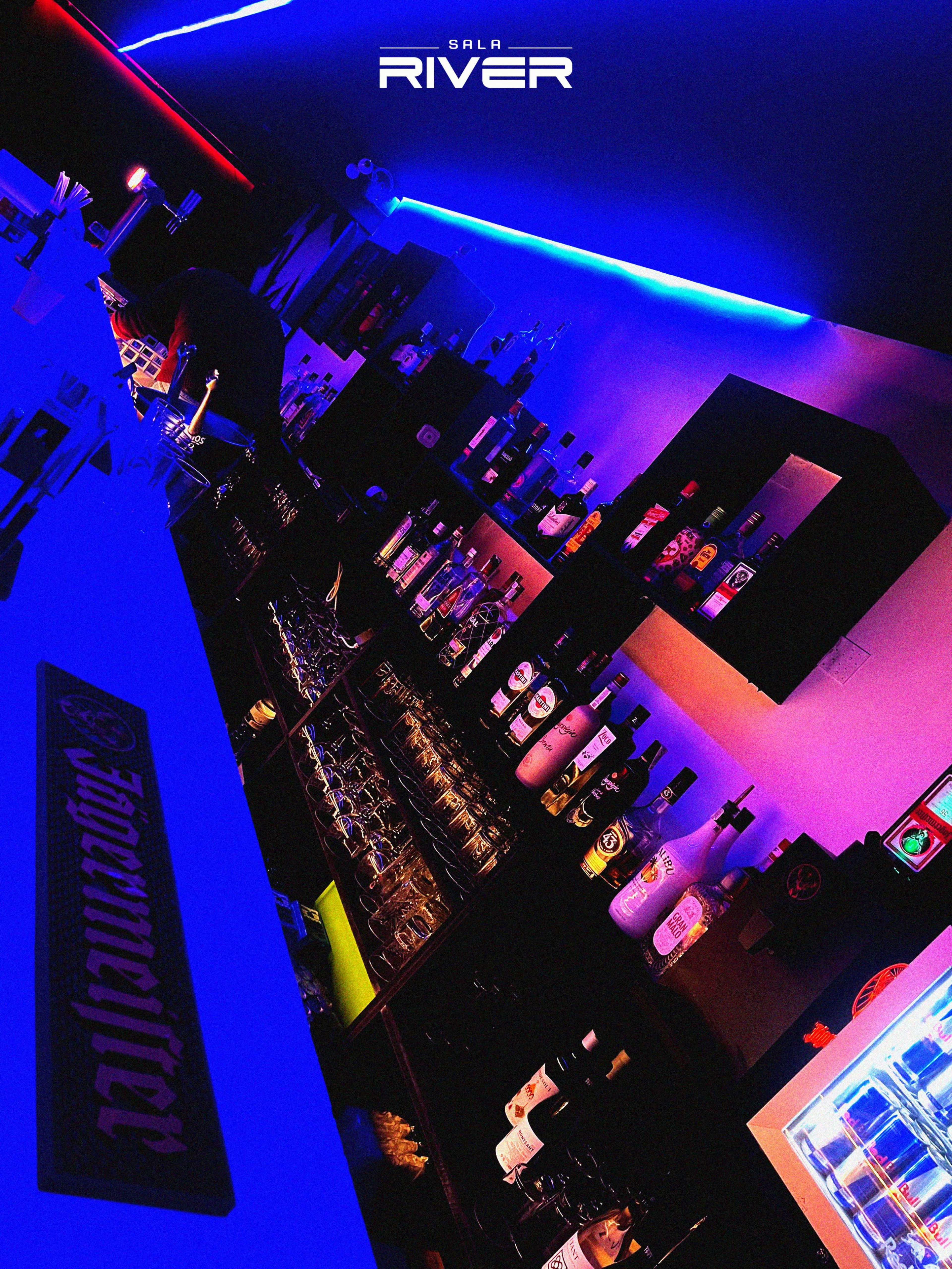A bar with illuminated shelves filled with various bottles of liquor against a backdrop of blue and purple lighting.
